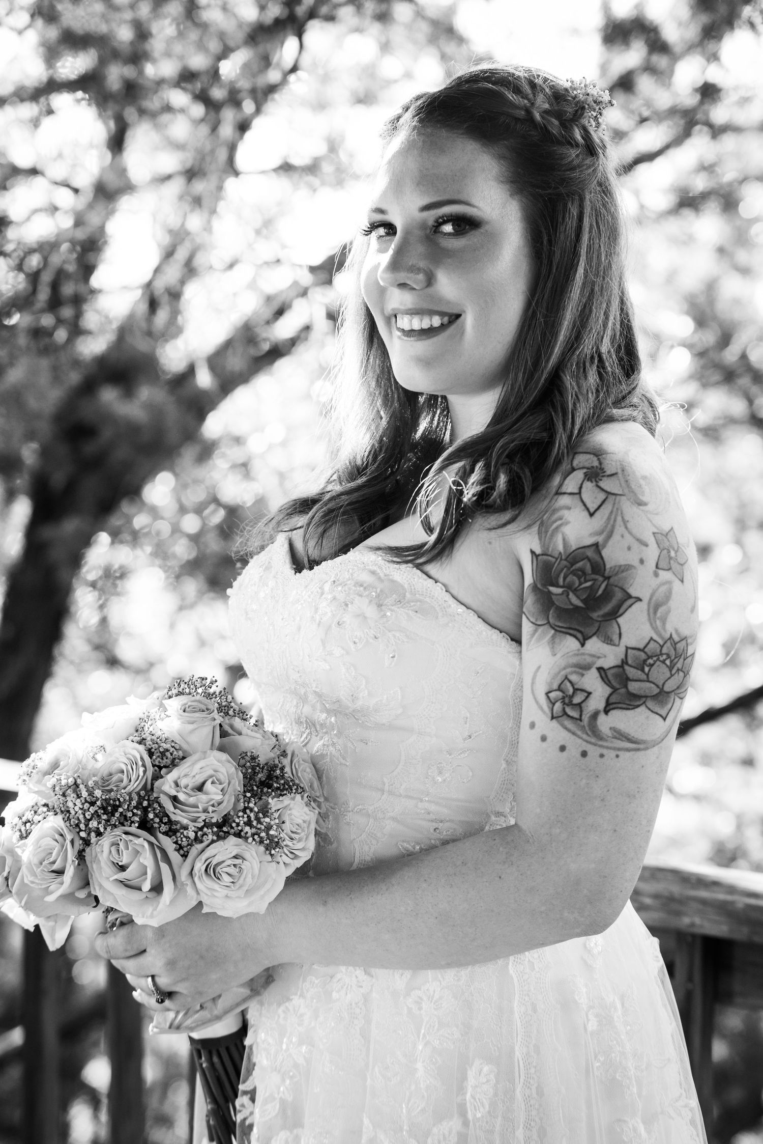 A bride in a white lace dress holds a bouquet of roses among trees.