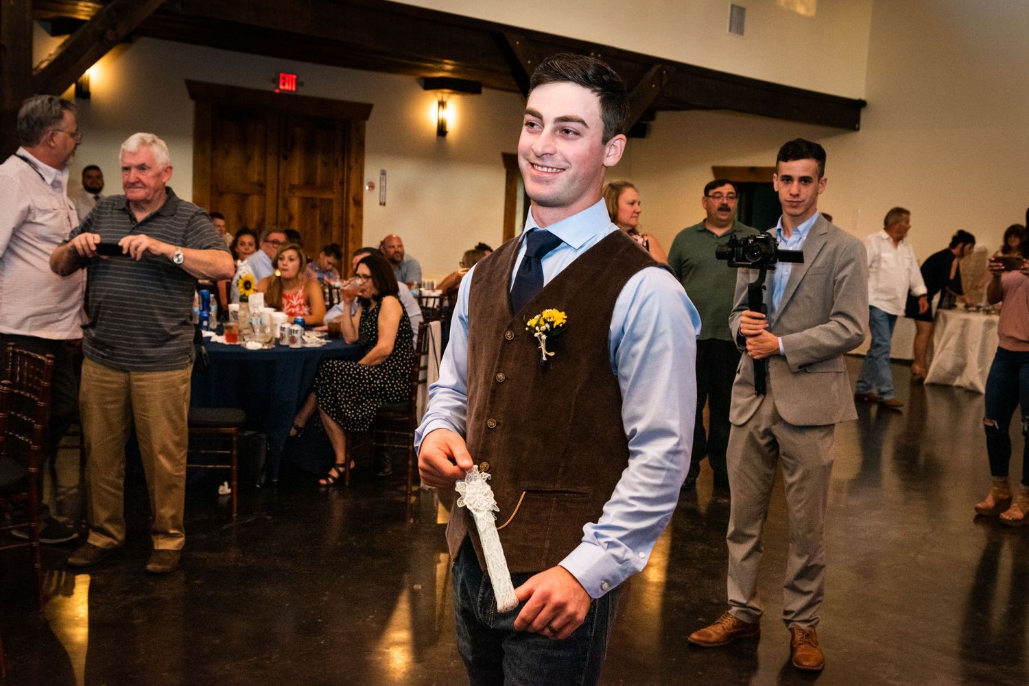 Wedding reception guest in vest holds bottle during celebratory moment.