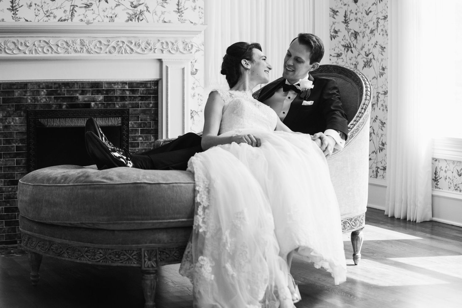 A black and white wedding portrait showing a tender moment on an antique chaise lounge.
