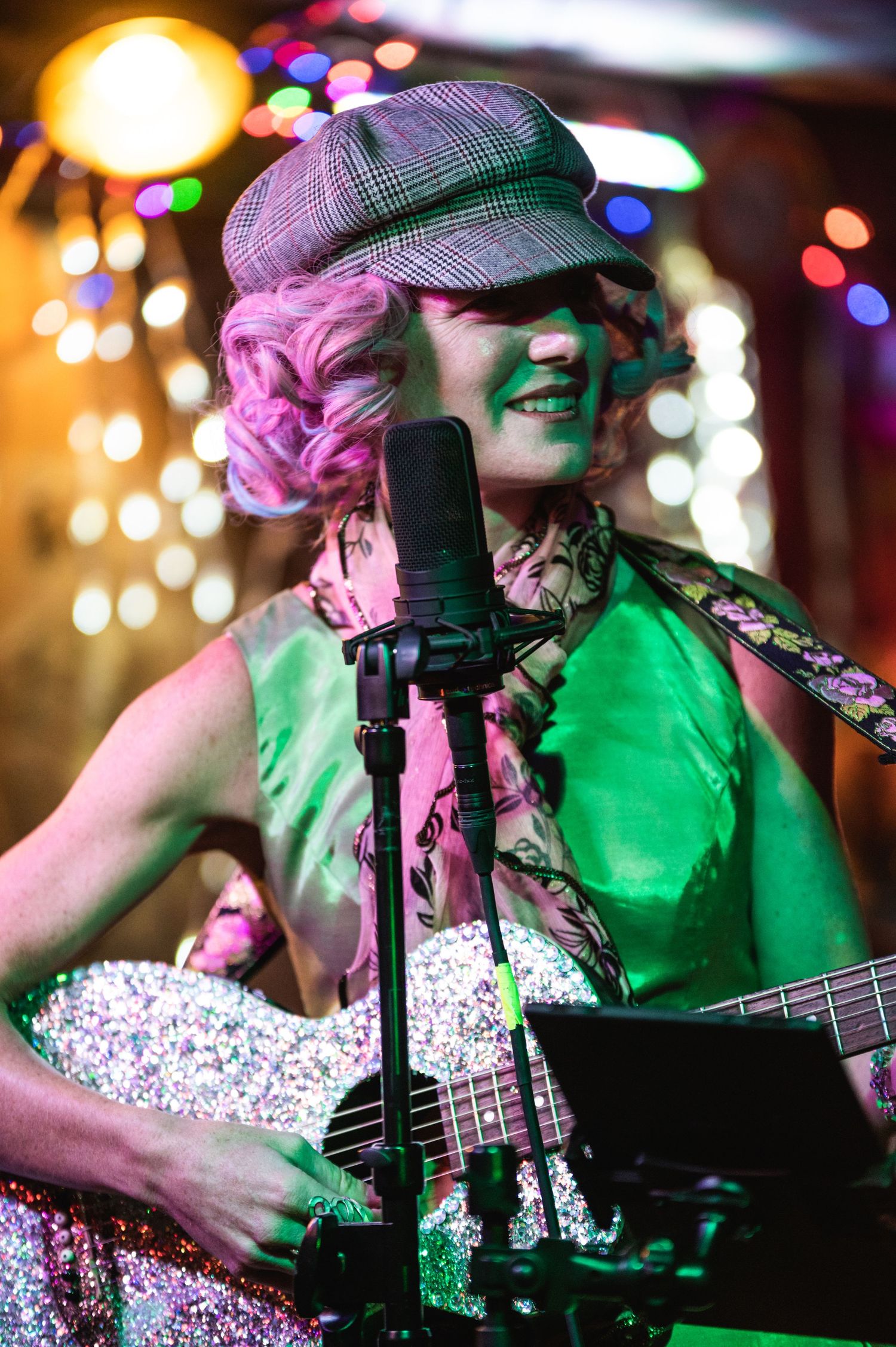 A performer in a newsboy cap plays guitar under vibrant stage lights with bokeh effects.