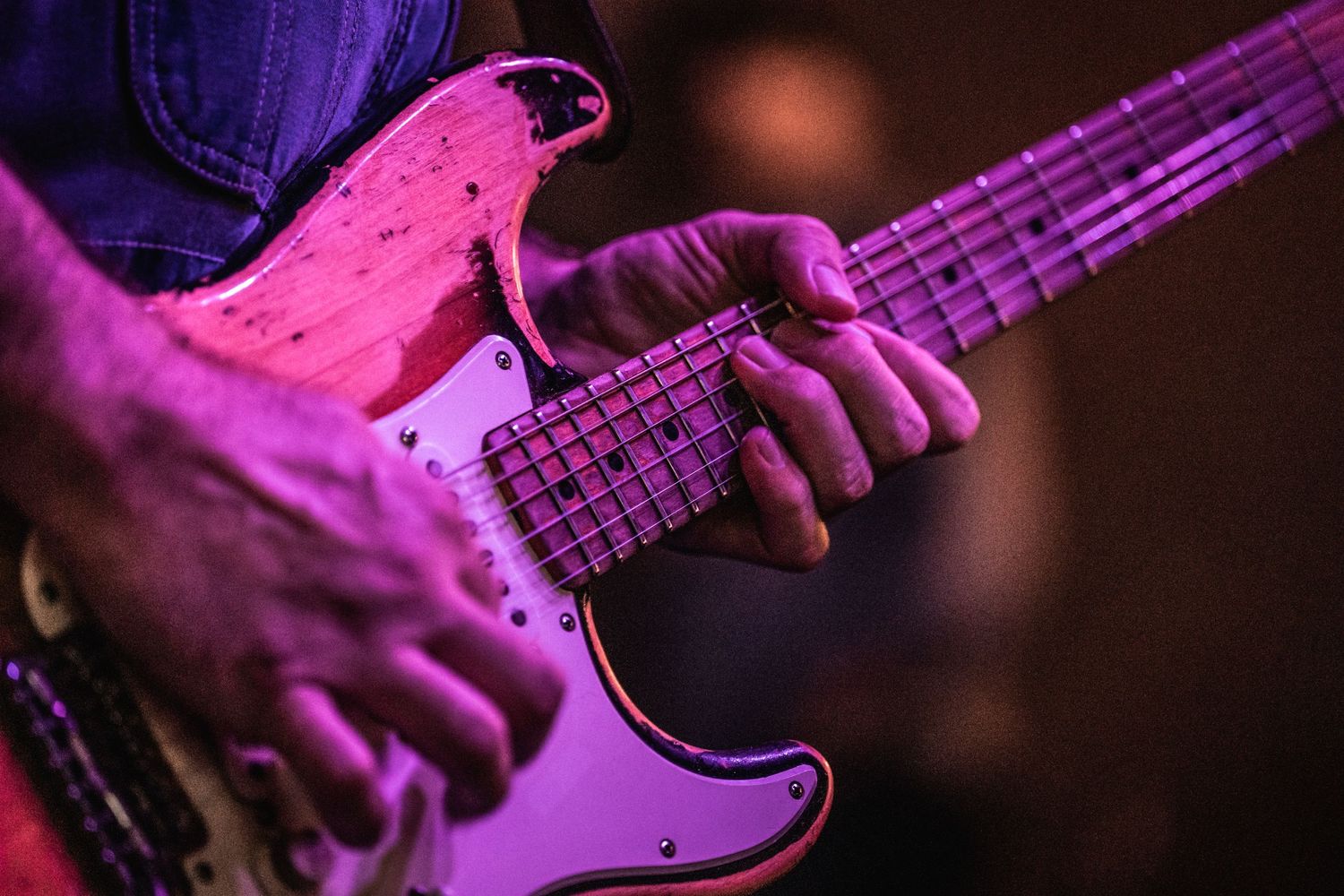 Close-up shot of hands playing an electric bass guitar under purple stage lighting.