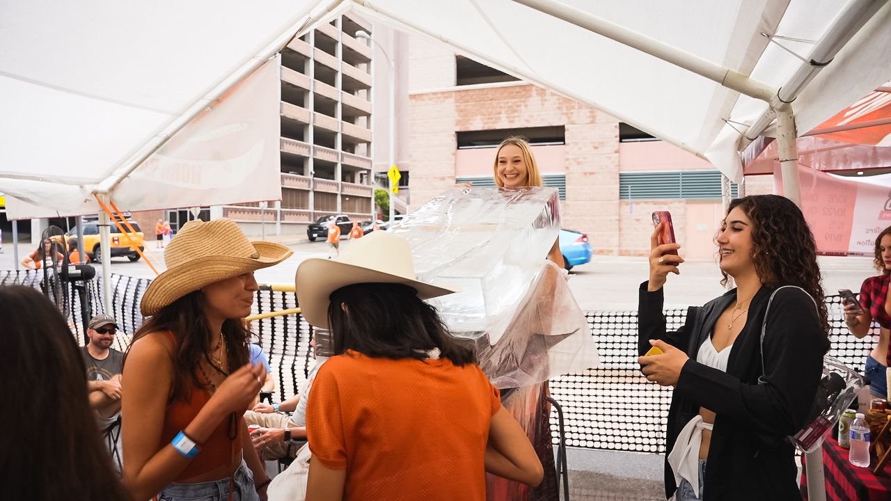 Party attendees in cowboy hats enjoying drinks under white tent at outdoor celebration.