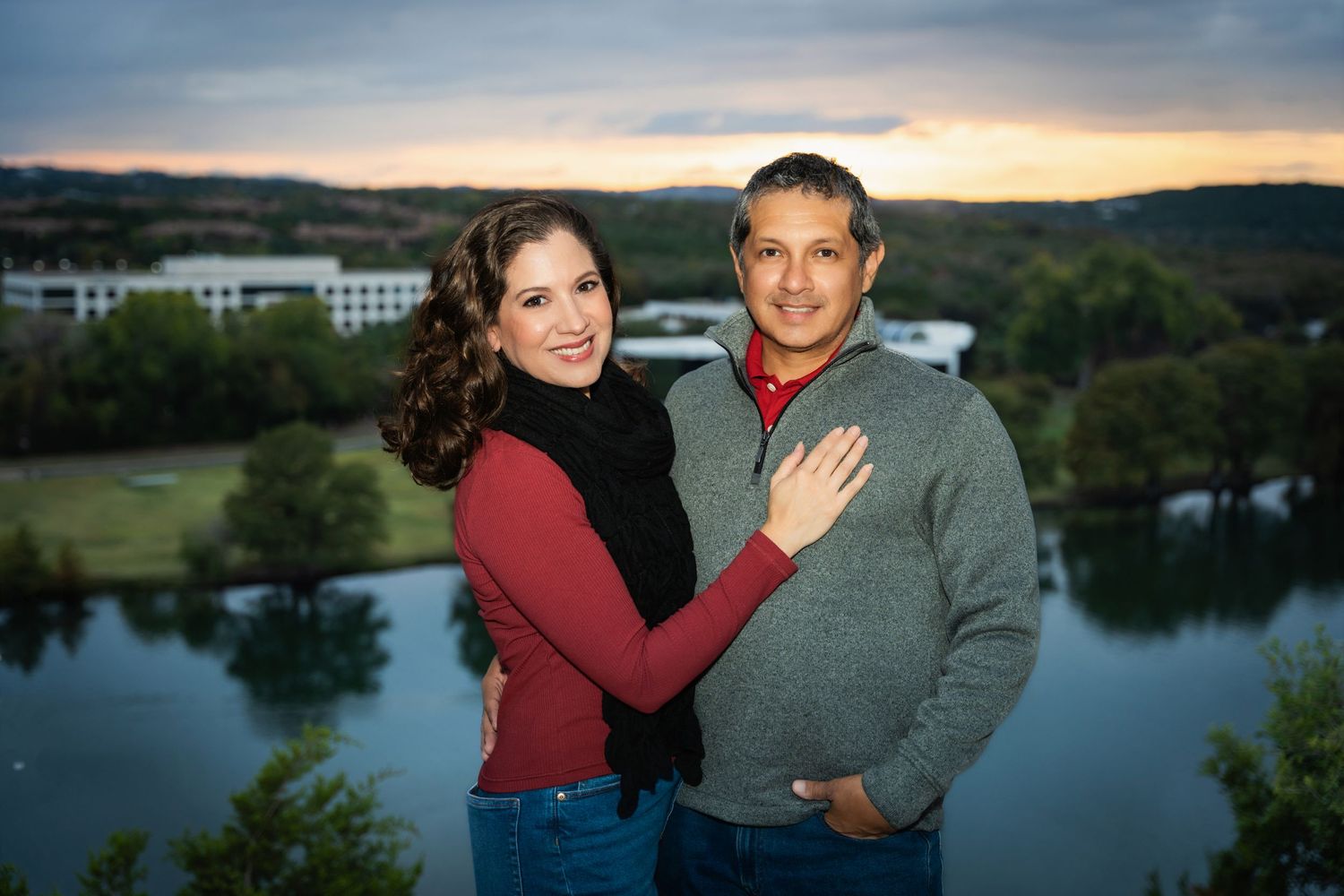 Couple posing together outdoors at sunset with a lake and rolling hills in the background.