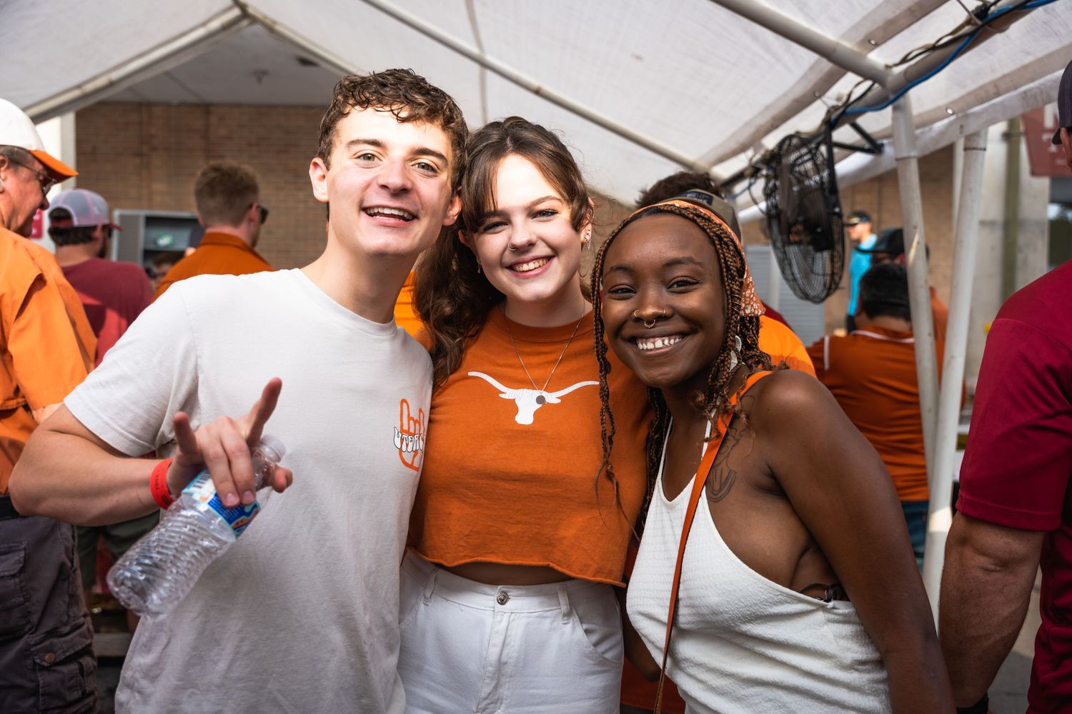 Three friends in Texas Longhorns gear celebrate together at an outdoor event.