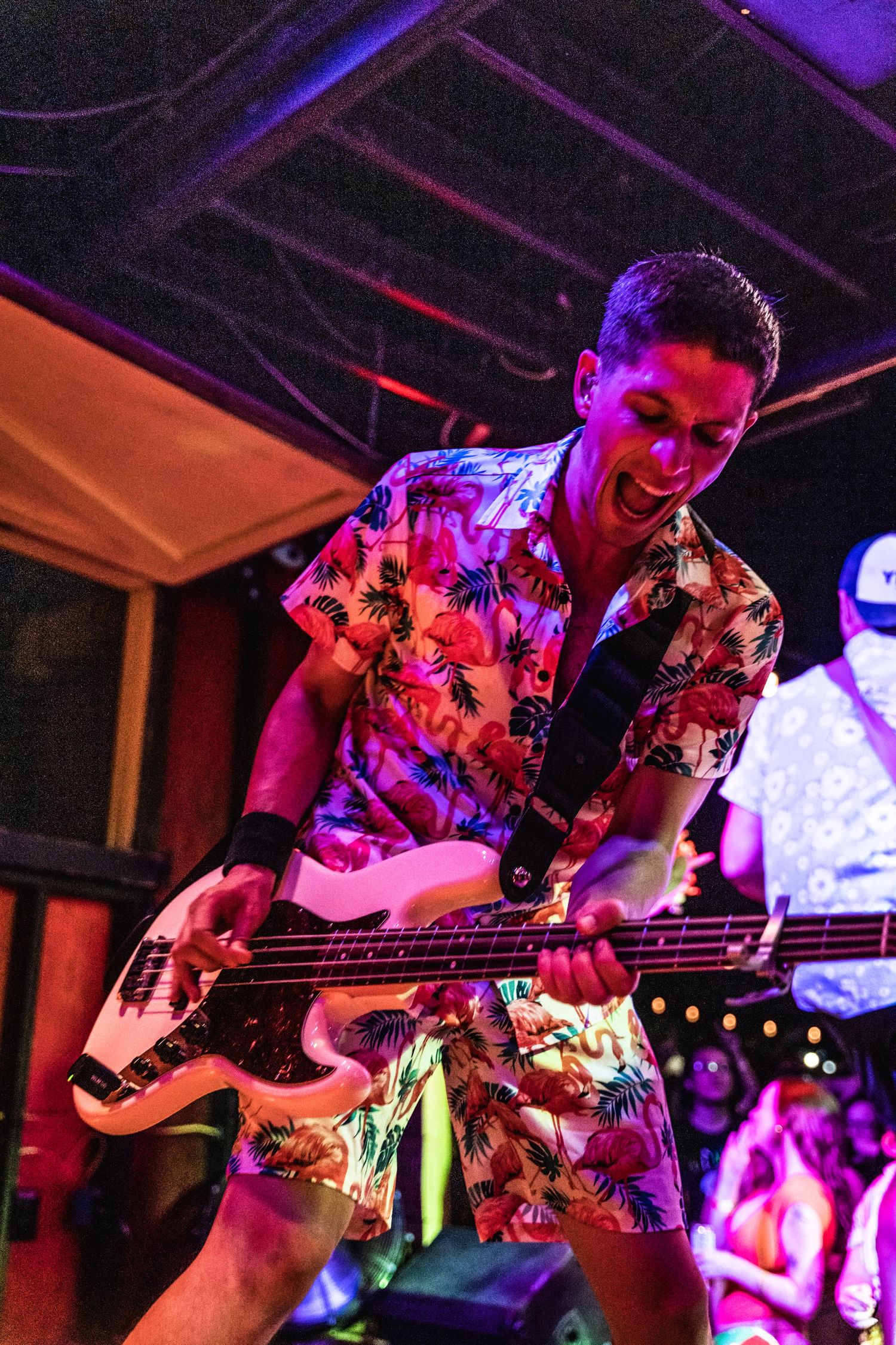 Bass guitarist in floral shirt performing under colorful stage lights.