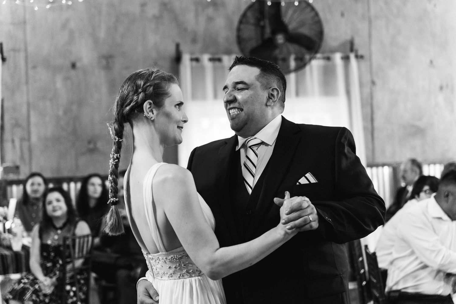 Black and white photo captures an intimate first dance moment at an indoor wedding reception.