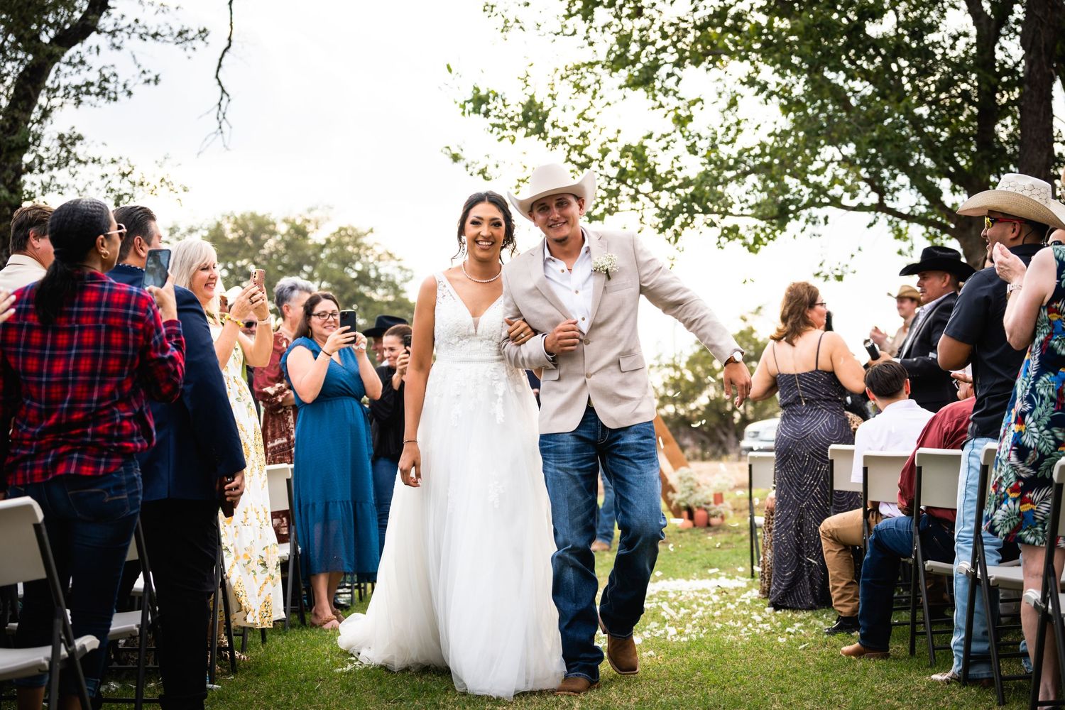 Newlyweds walk down the aisle together at outdoor ceremony while guests celebrate.