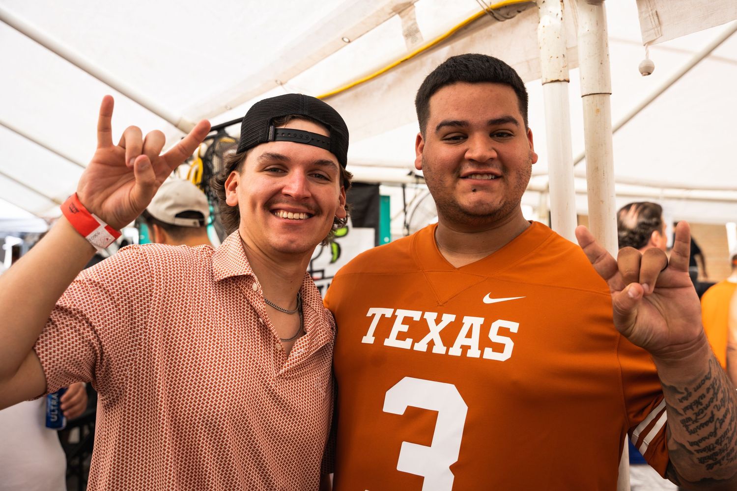 Two college sports fans pose together showing Texas Longhorns pride at a tailgate event.