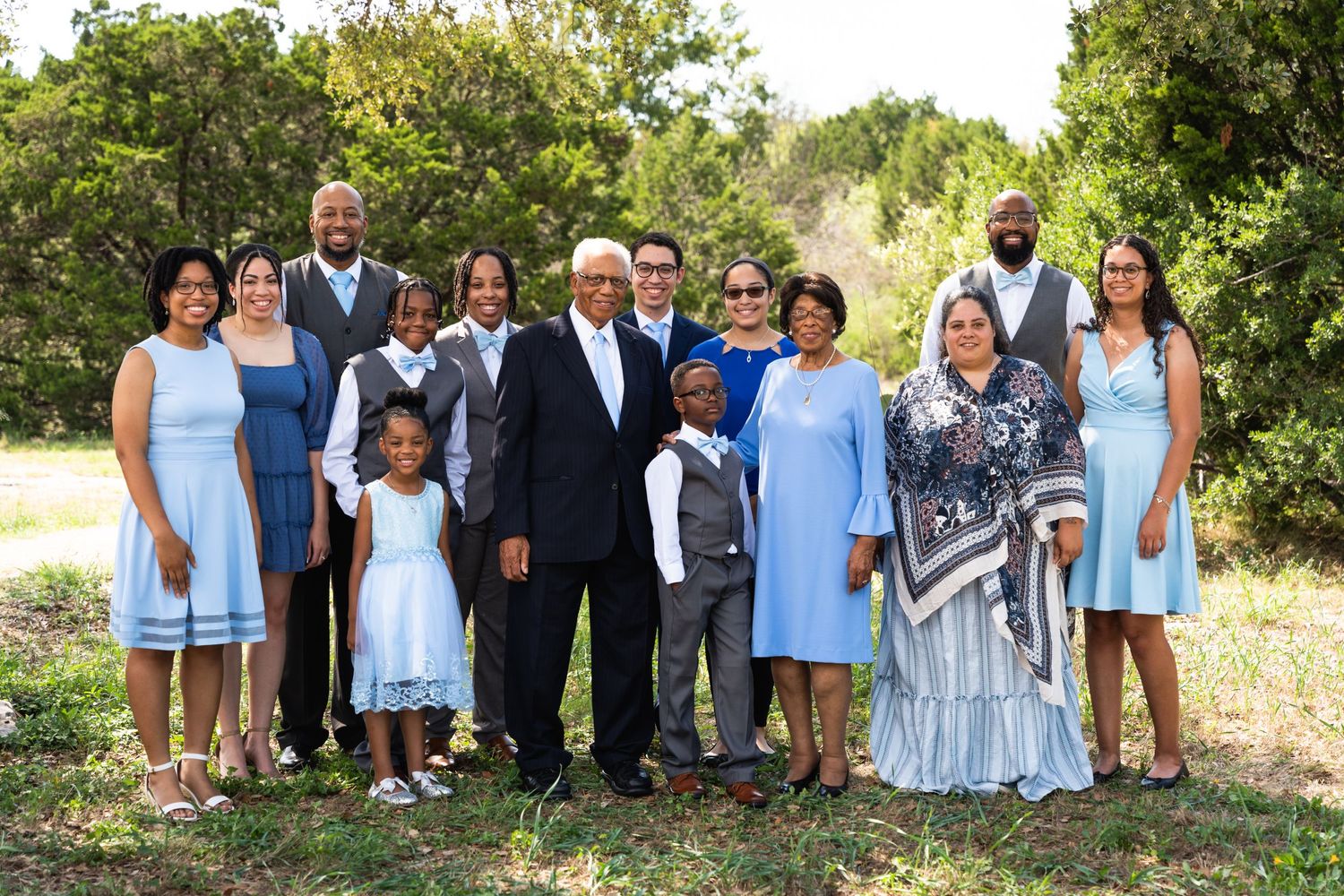 Large family gathering in coordinated blue and white outfits for formal outdoor photo.