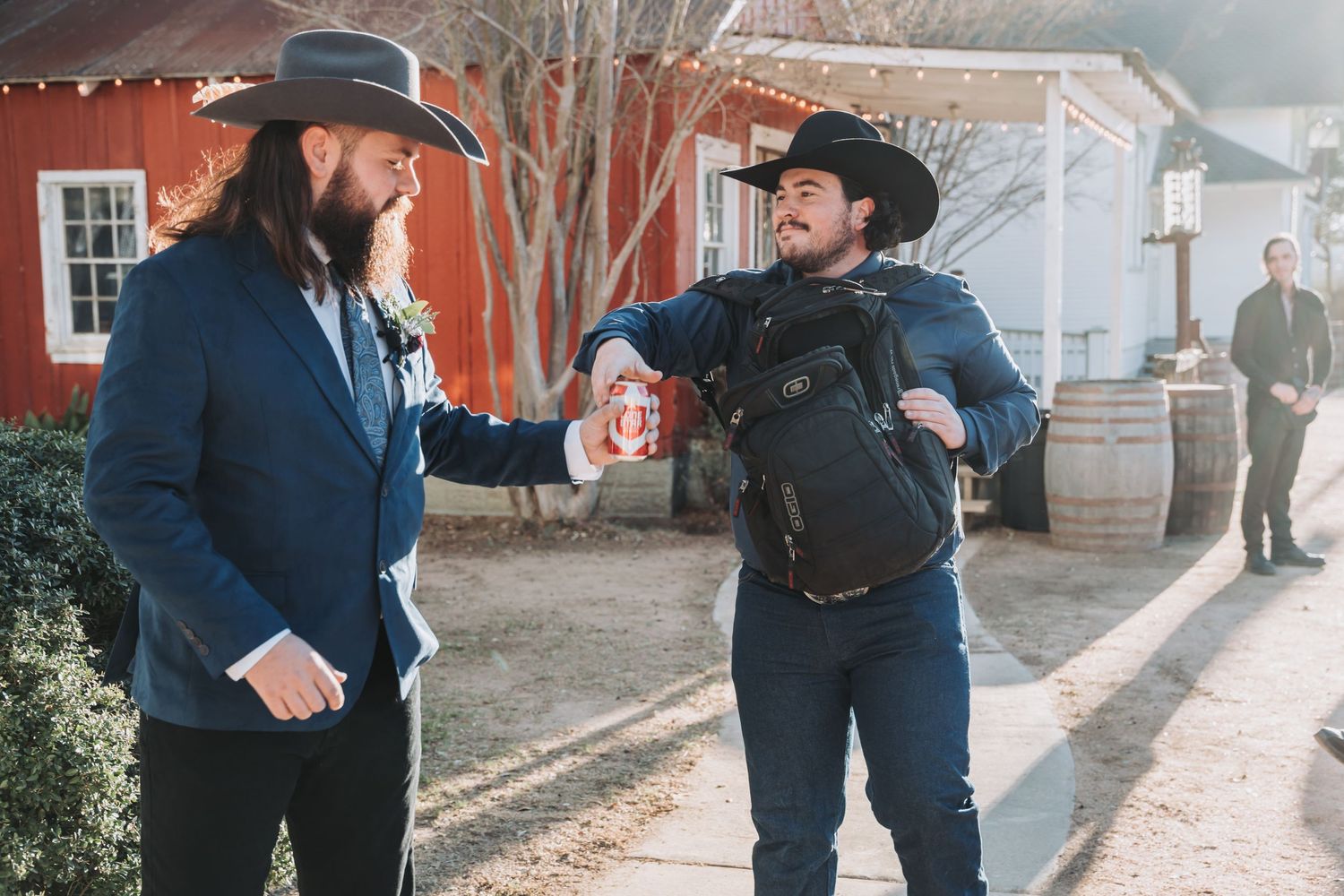 Two people in western attire share a lively moment in front of a red building.