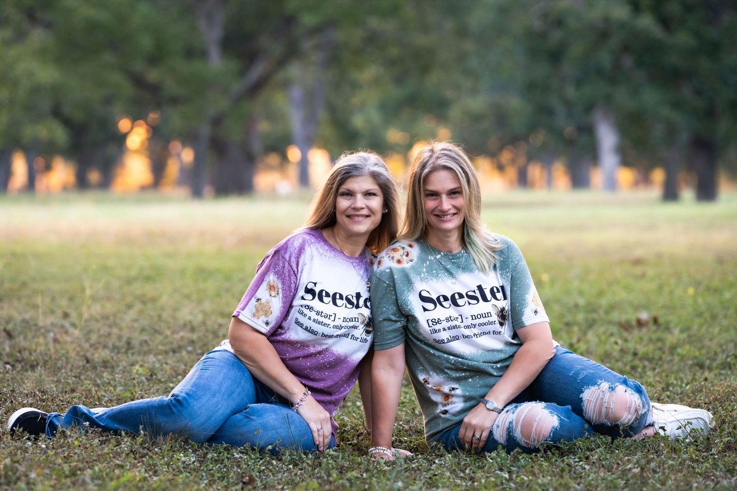 Two friends in coordinating t-shirts sitting together on grass during golden hour.