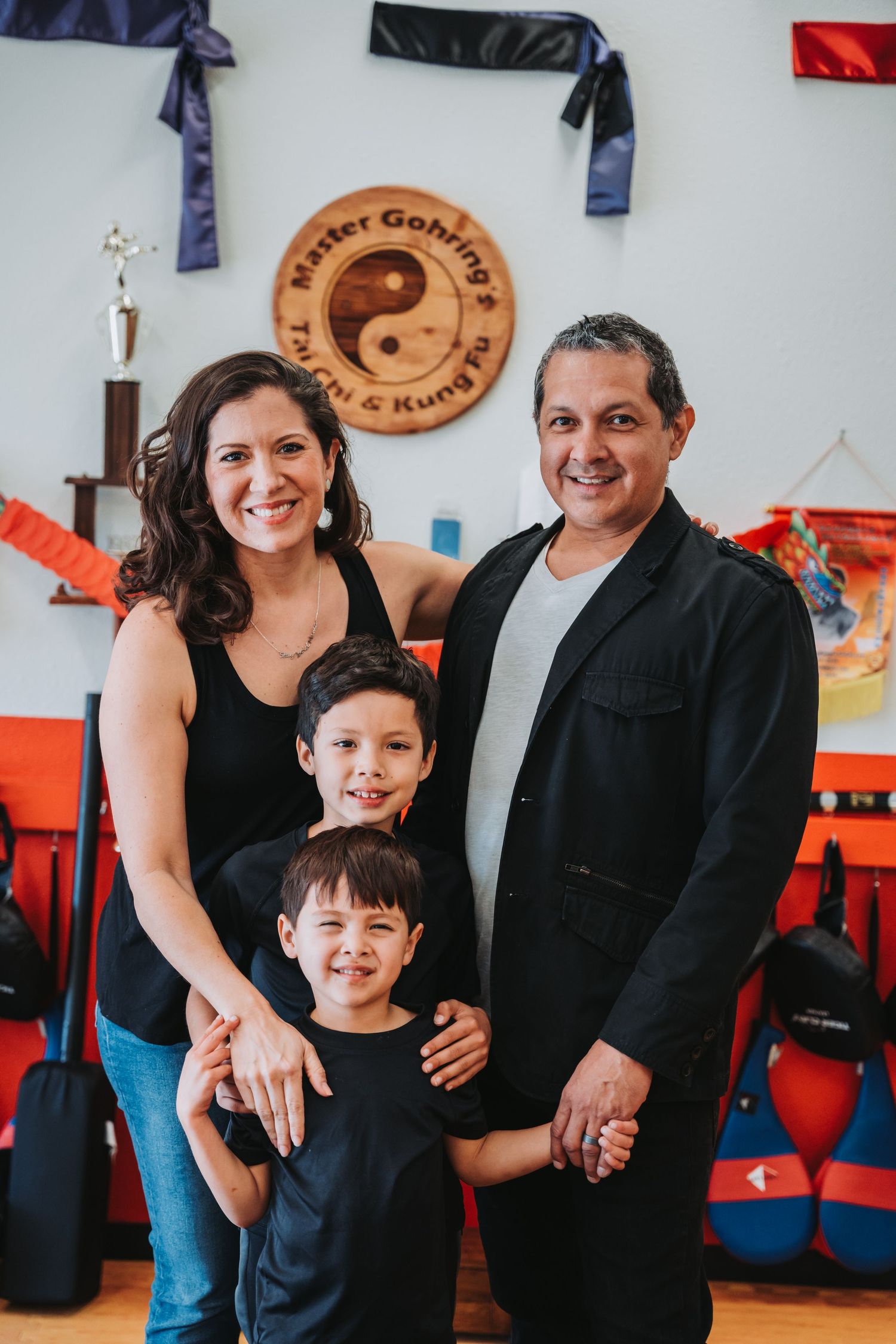 Family portrait in martial arts studio with yin yang symbol and belts on wall.