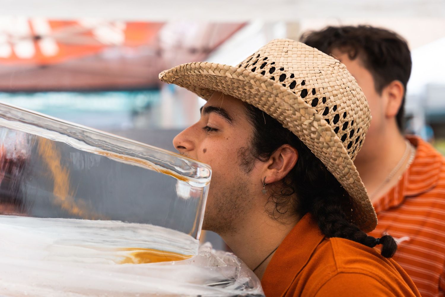 Person wearing a straw hat drinks from a tube at an outdoor party event.