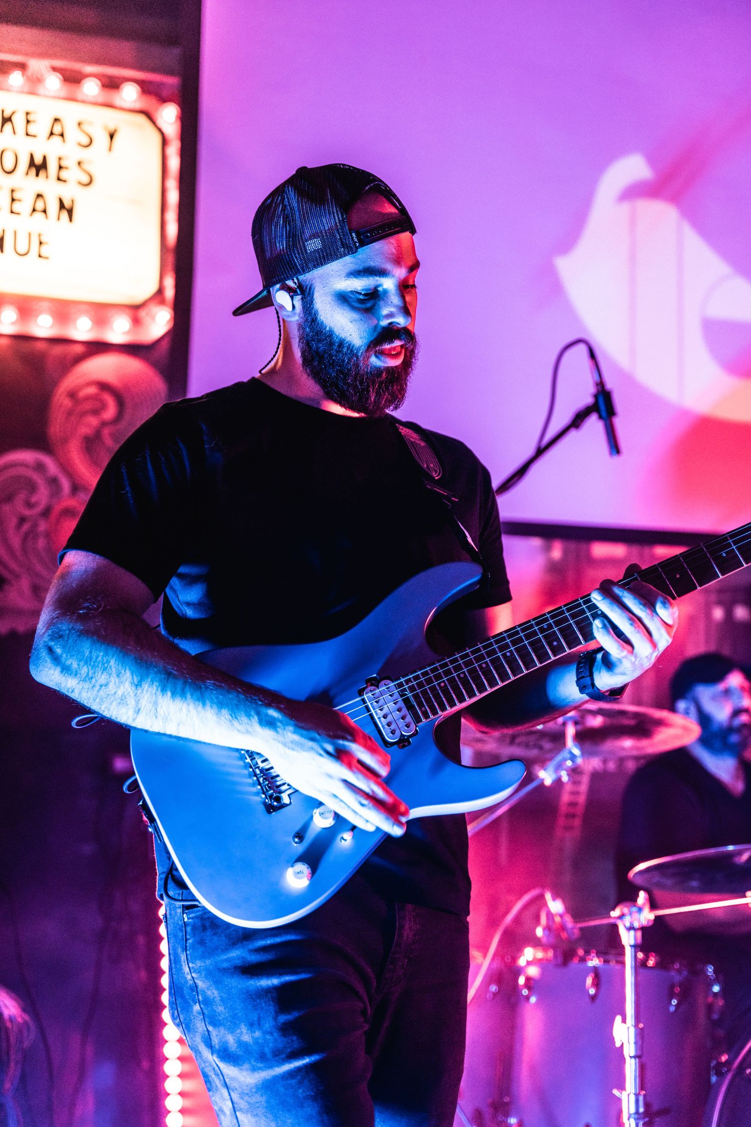 Guitarist in black attire performs under dramatic blue and purple stage lighting.