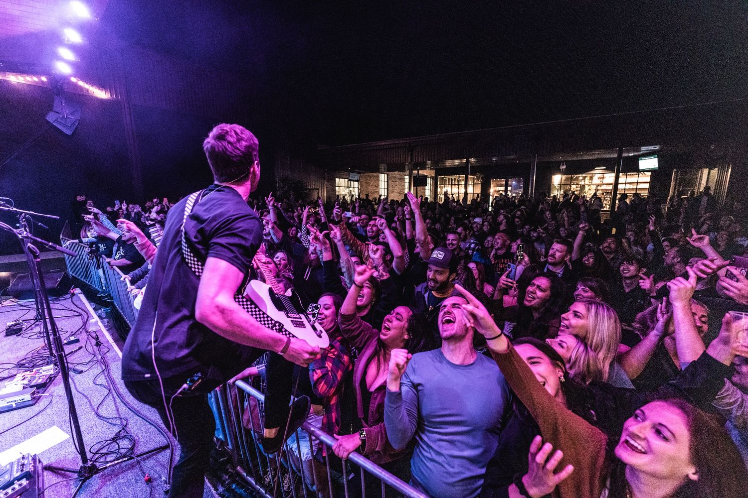 Concert crowd cheers as performer plays on stage with purple lighting effects.
