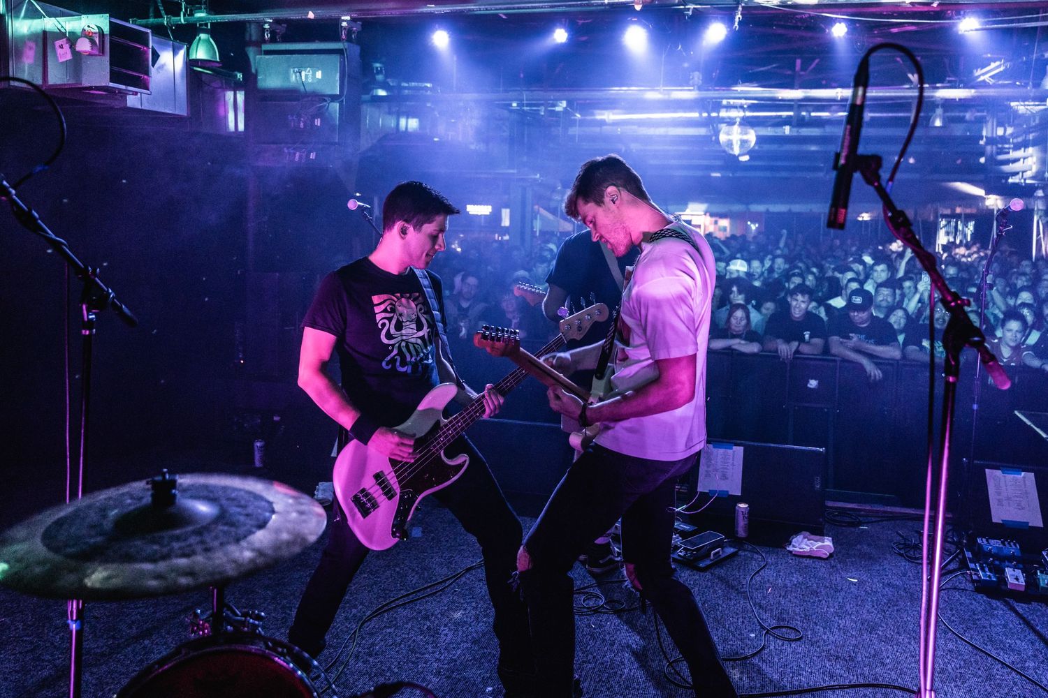 Two guitarists performing on stage under blue concert lighting.
