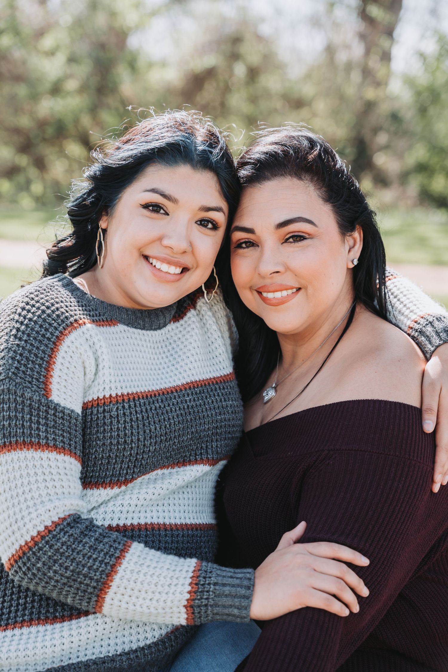 Two people in sweaters smiling together outdoors with natural lighting.