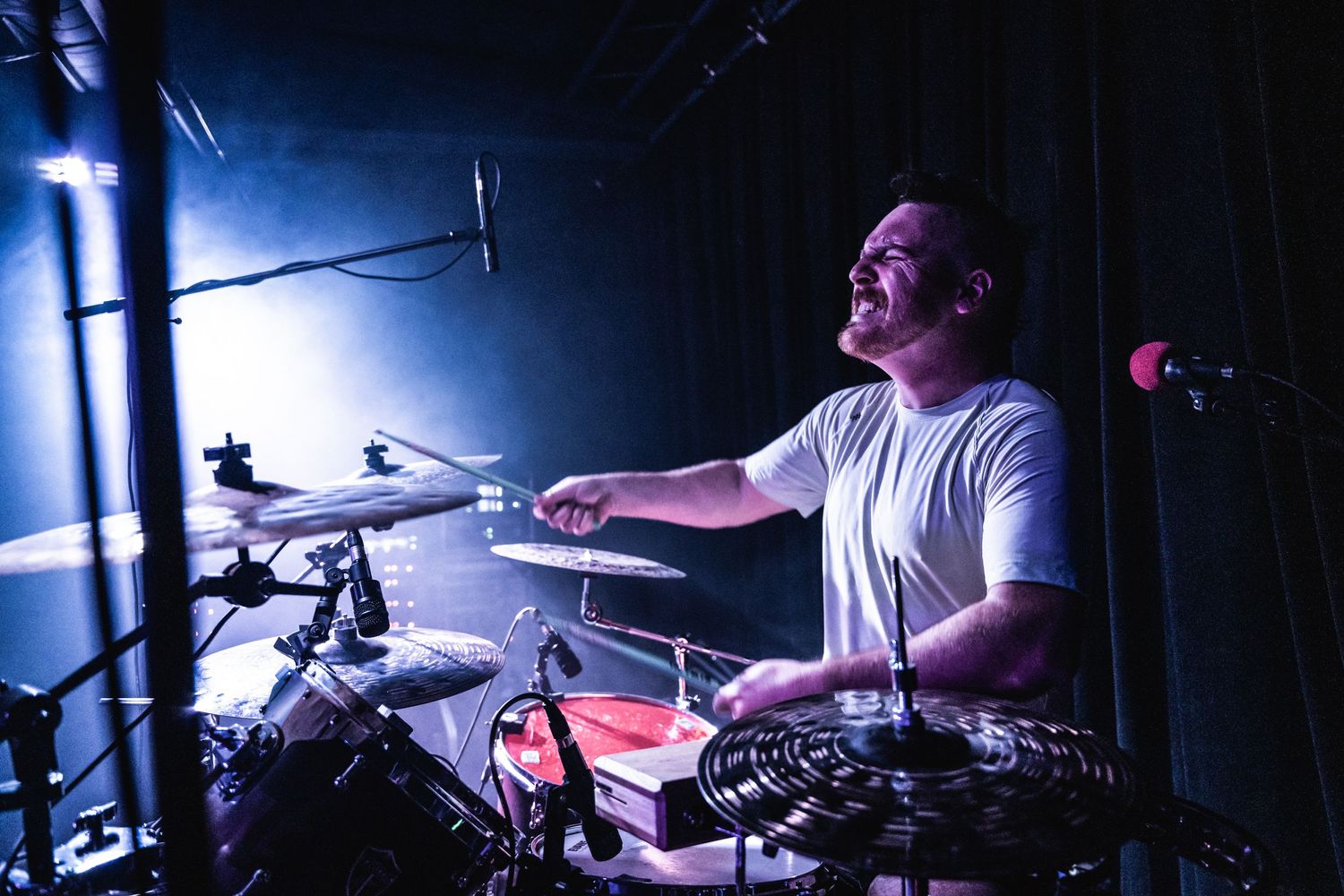 Drummer performs energetically under dramatic blue stage lighting during a concert performance.