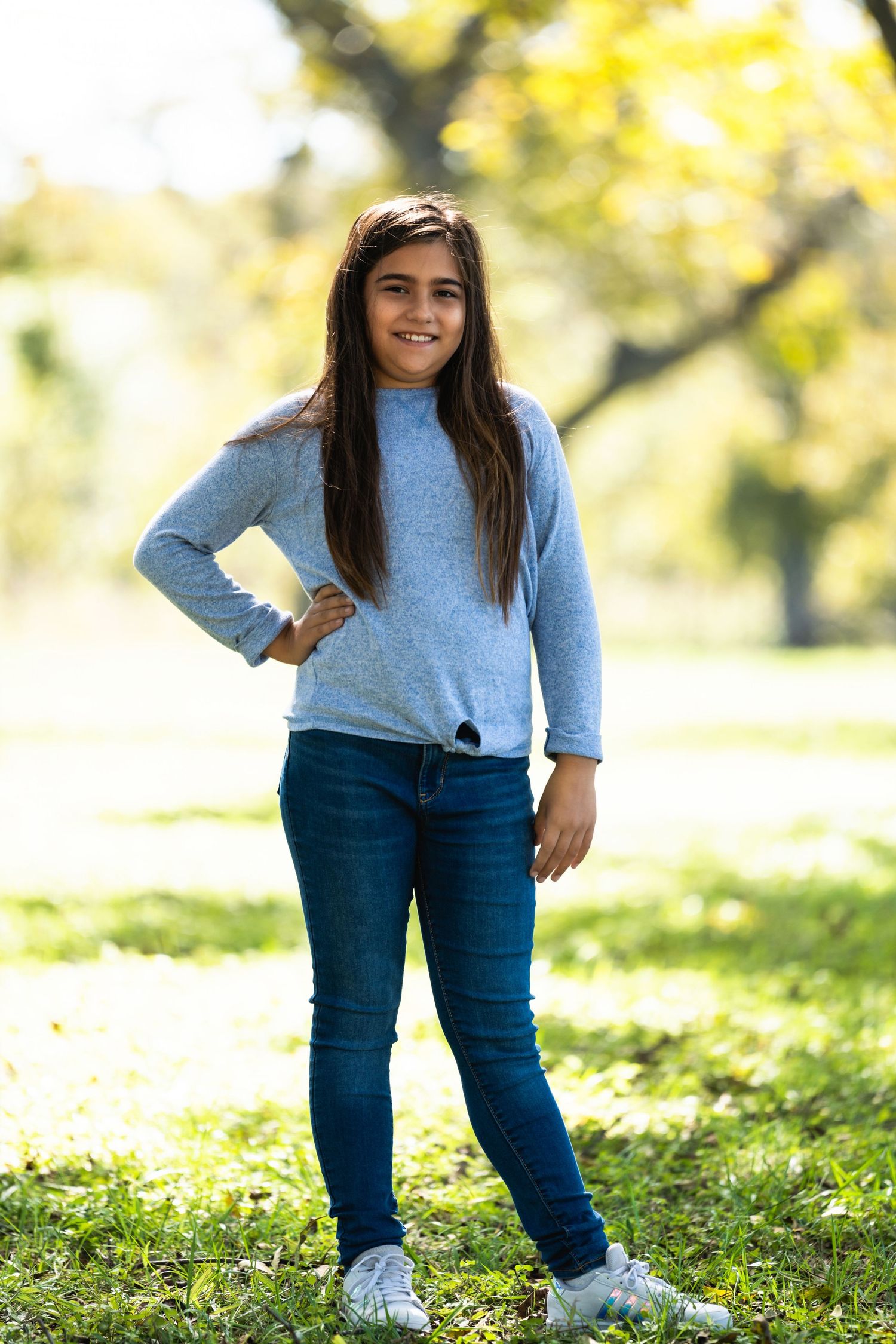 Young person in blue sweater and jeans poses outside during autumn.
