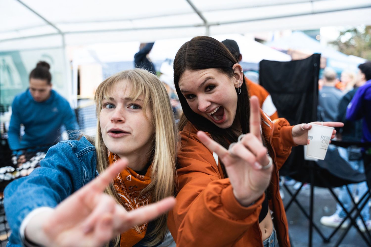 Two friends posing with enthusiastic expressions under a white tent.