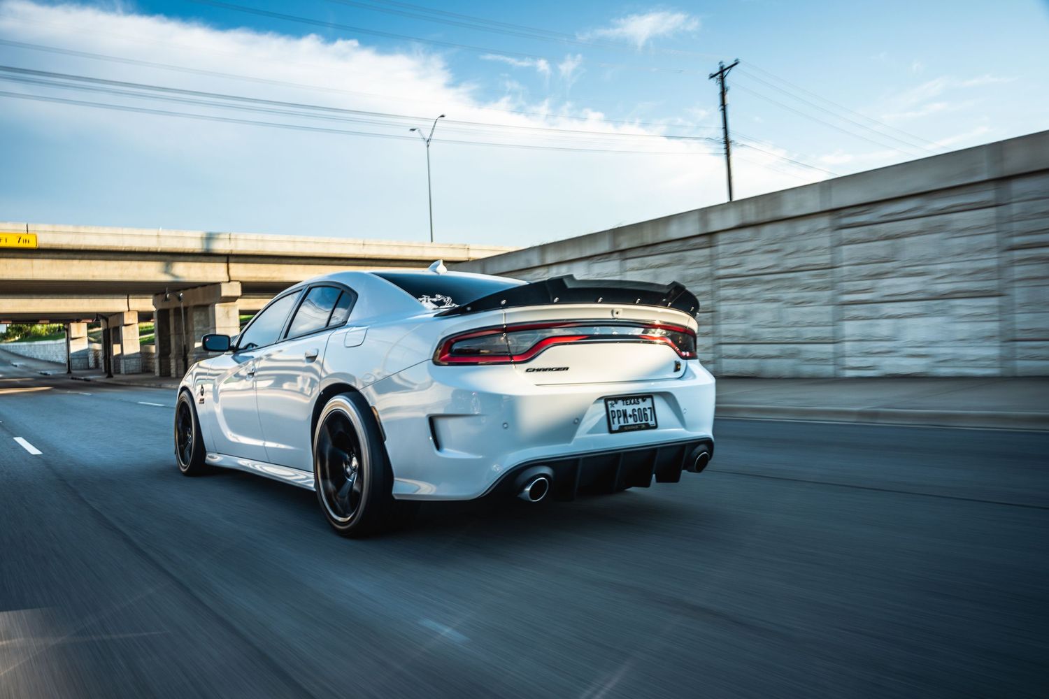 White Dodge Charger with rear spoiler photographed in motion near concrete wall.
