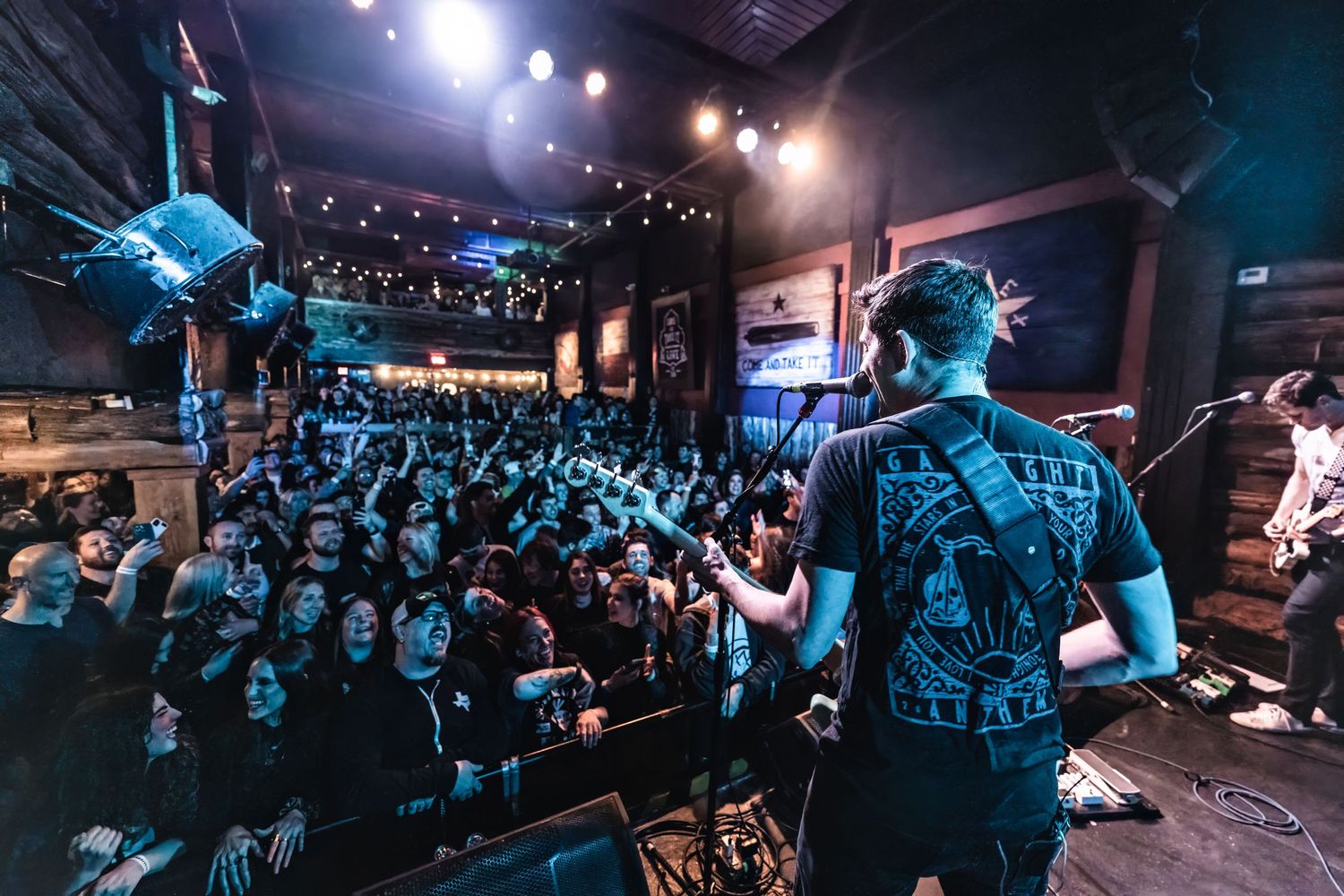 Musician performs to packed crowd in dimly lit concert venue with blue stage lighting.
