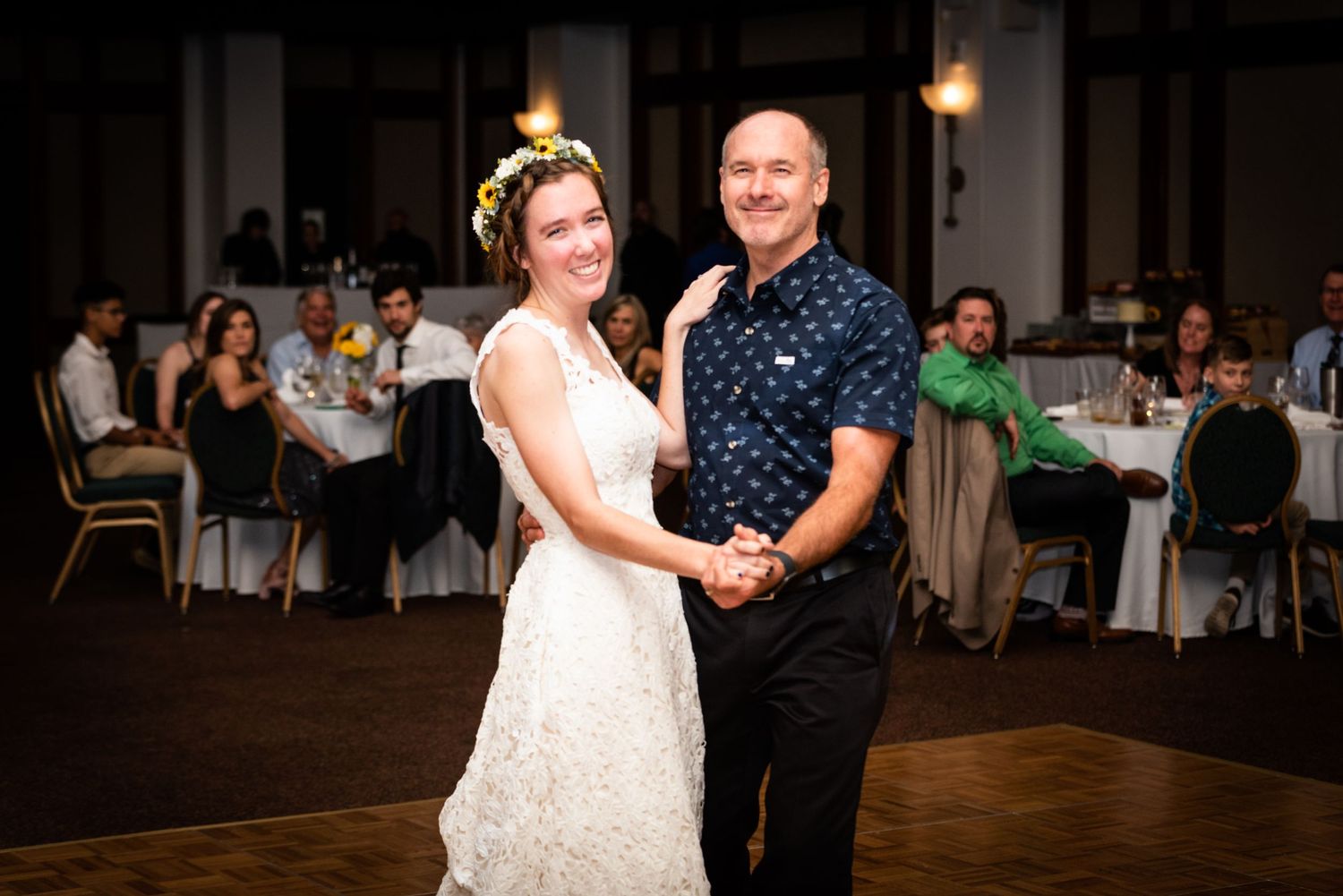 A couple stands together during their wedding reception on a wooden dance floor.