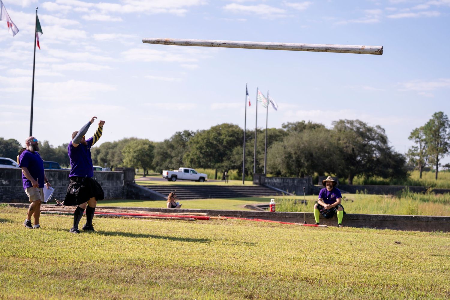 People launching model airplanes on a grassy field with flags and trees in the background.