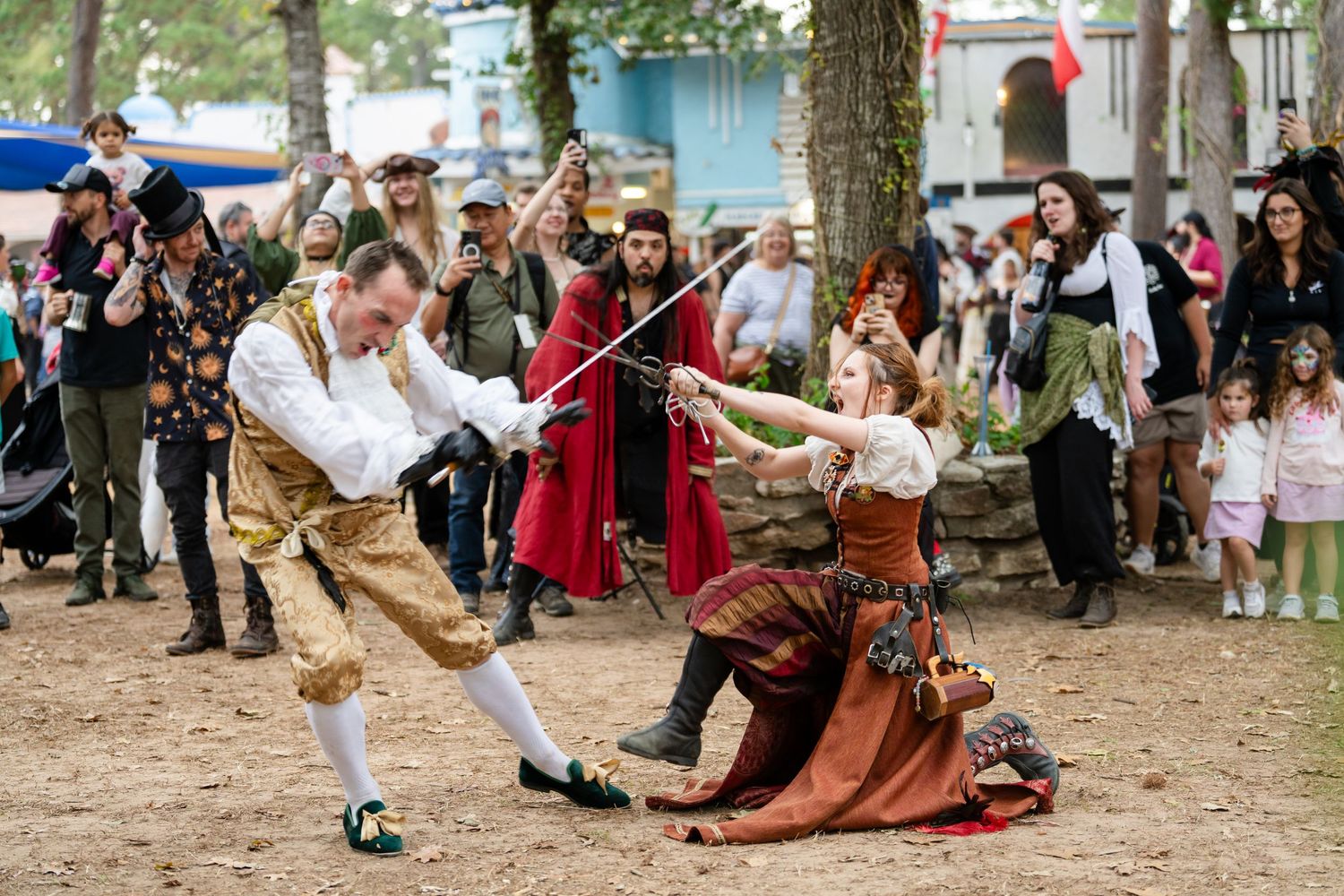 Medieval performers in period costumes demonstrate traditional sword fighting techniques at a historical reenactment festival.