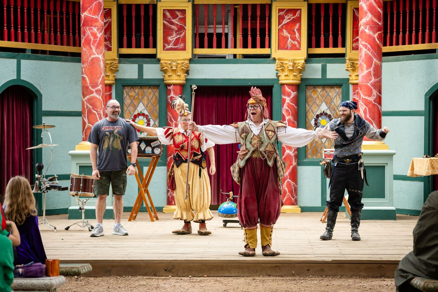 Performers in traditional costumes stand on a wooden stage during an outdoor theatrical performance.