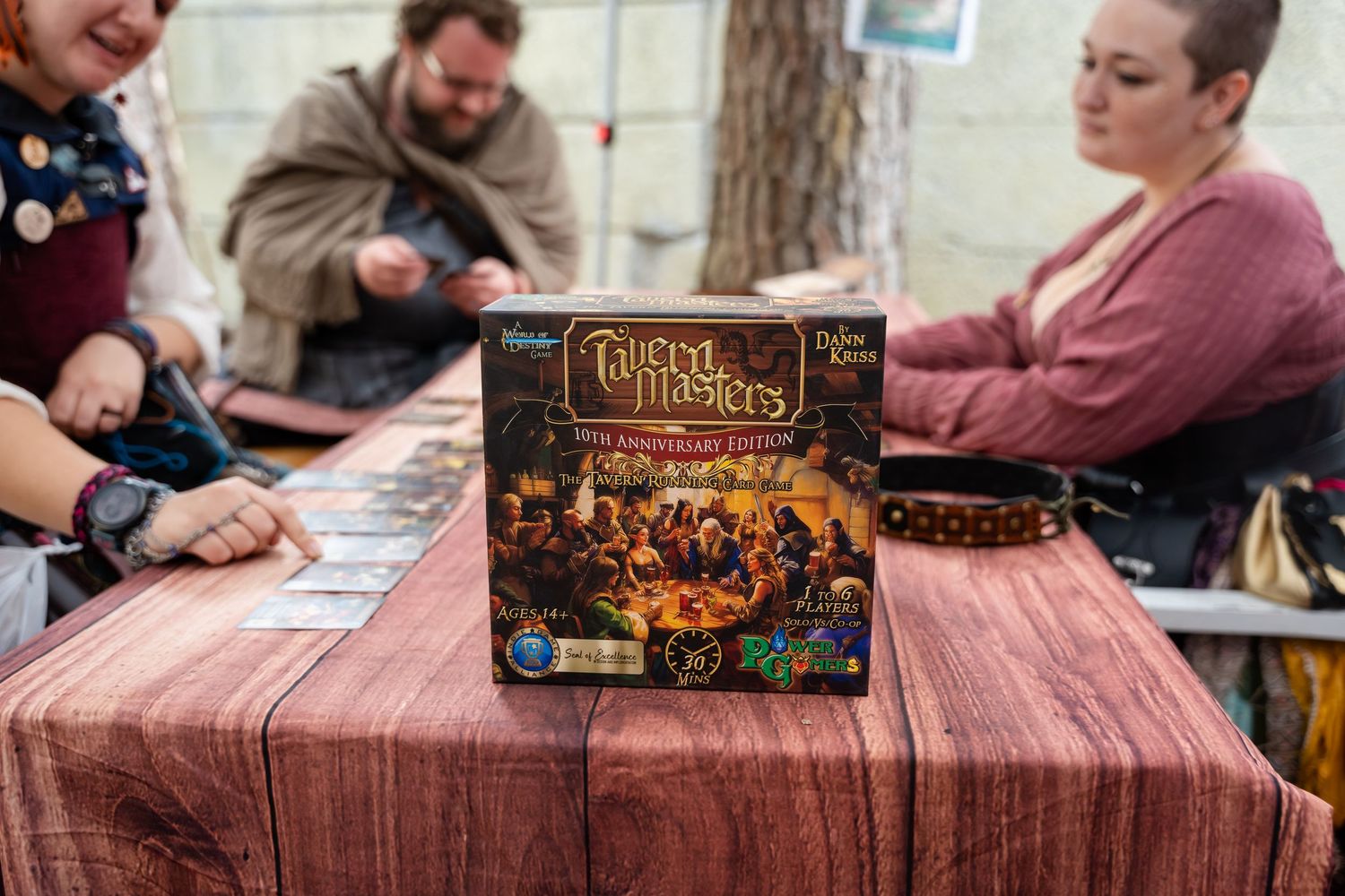 People gathered around a table playing a board game with game boxes and components visible in a social setting.