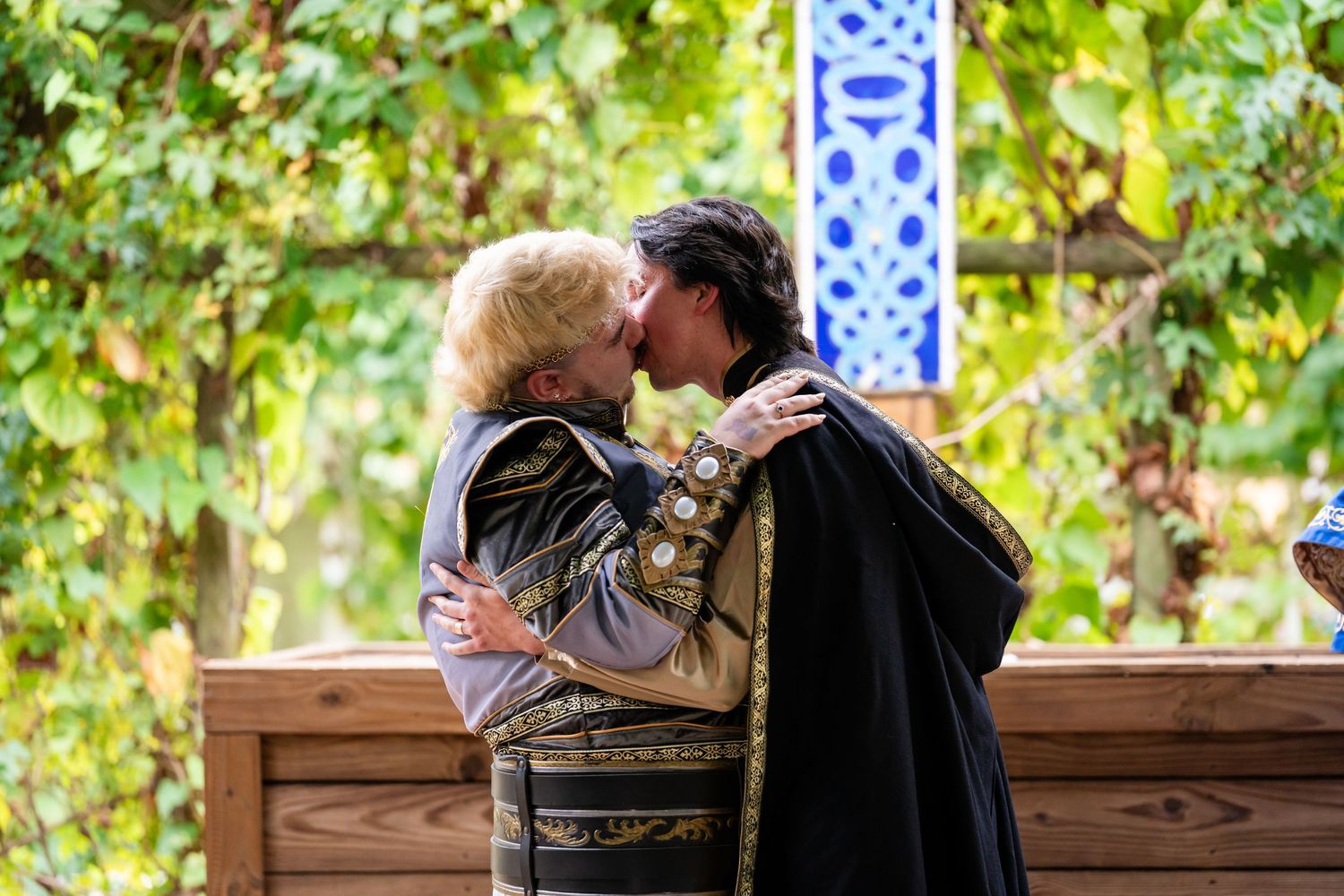 A romantic moment shared between two people in traditional attire at a garden gazebo surrounded by green foliage.