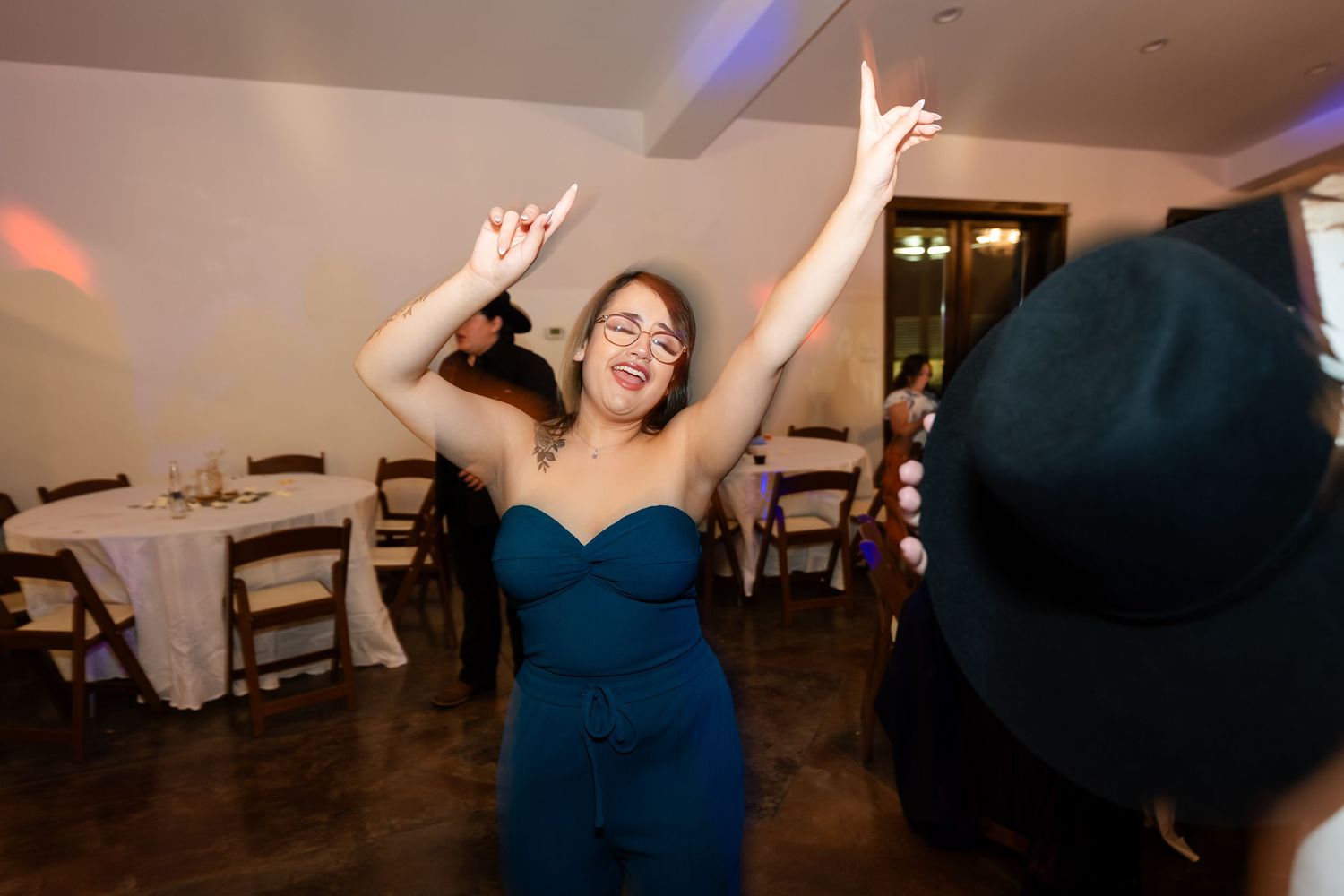 Woman in teal strapless dress dancing with arms raised at an indoor wedding reception celebration.