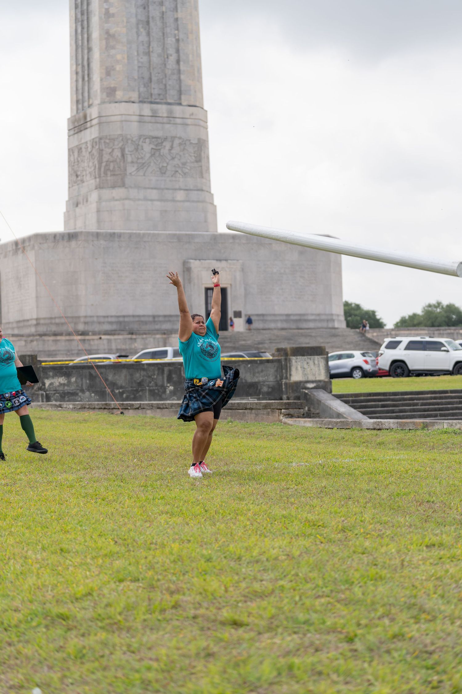Person in teal outfit dancing near a large stone monument on green grass under cloudy skies.