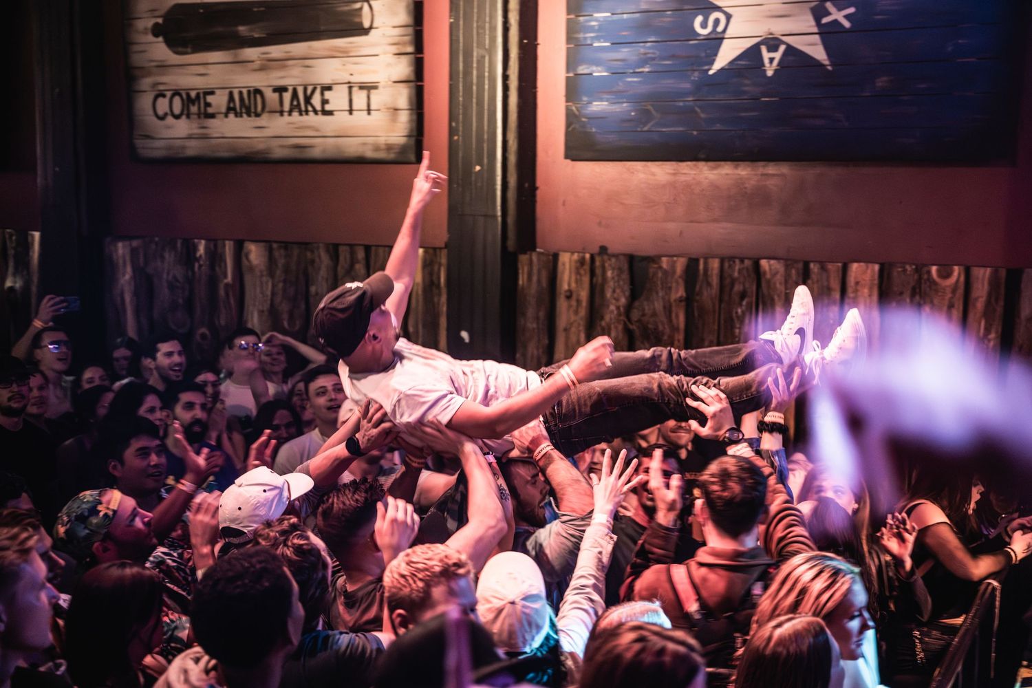 Concert crowd lifts a performer during an energetic show at a venue with a 