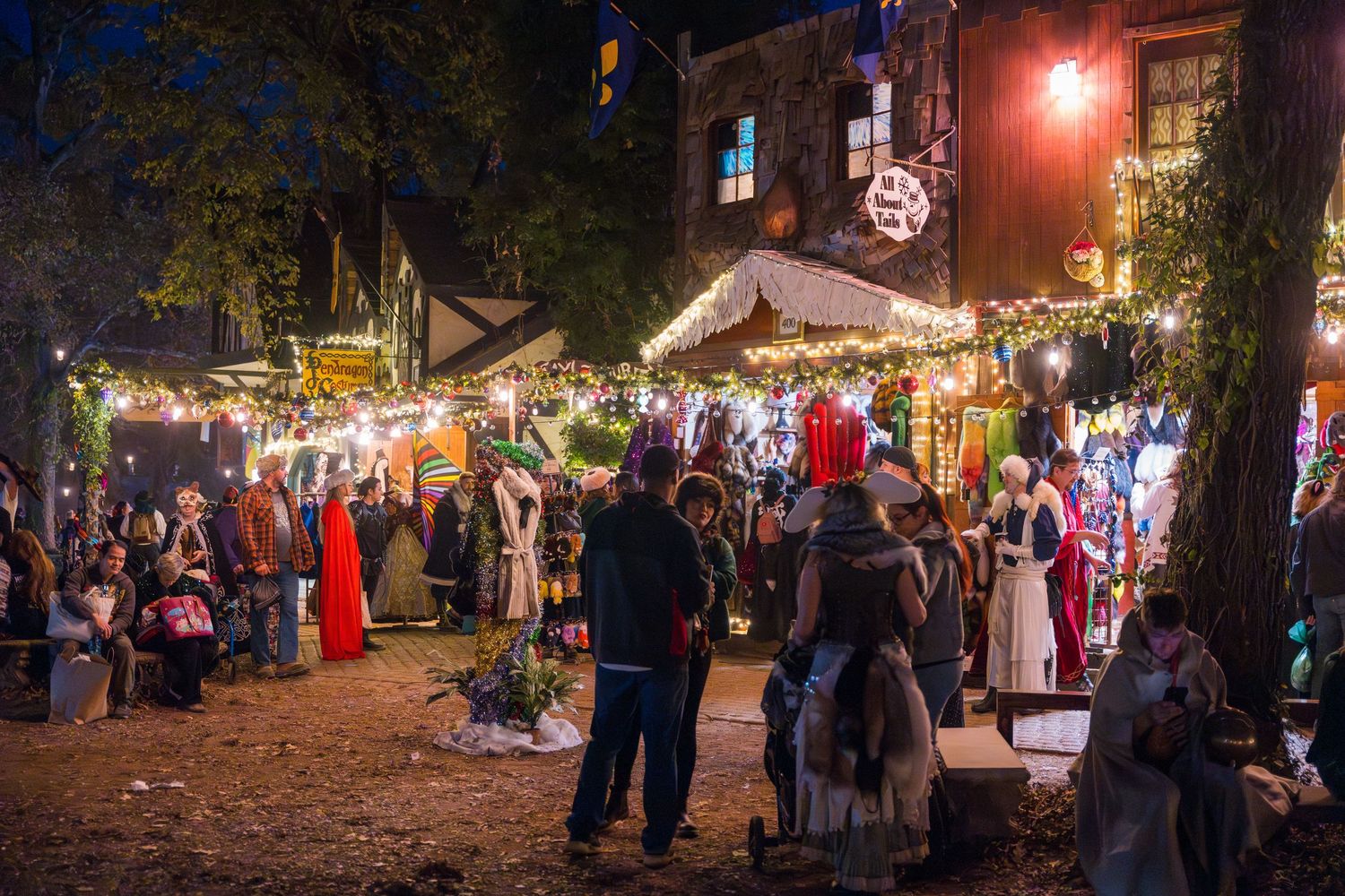 Festive outdoor holiday market at night with illuminated vendor stalls and shoppers browsing under twinkling lights.