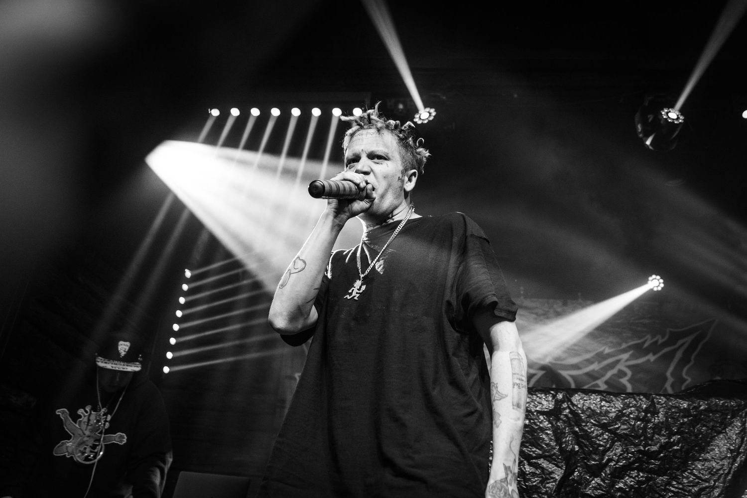 Concert performer in black shirt singing into microphone with dramatic stage lighting.