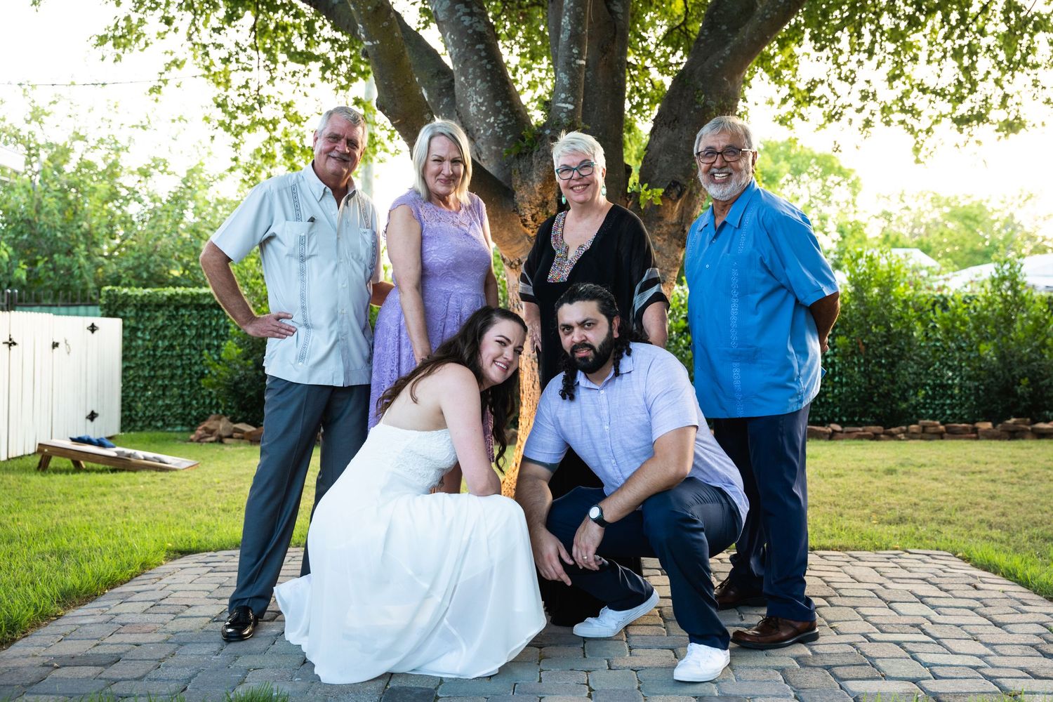 Small group poses for casual outdoor family photo under large tree.