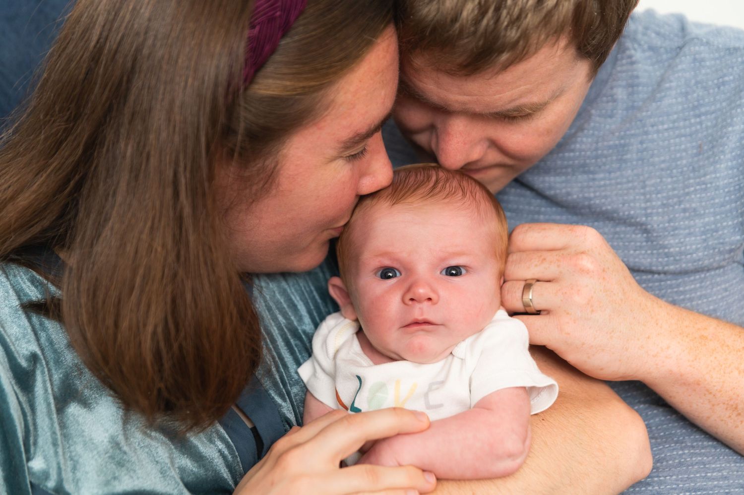 Close-up of tender family moment with young infant in parents' arms.