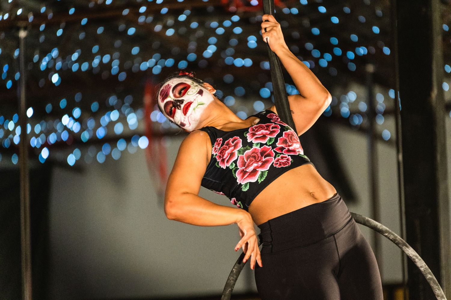 Performer in decorative makeup executes dance move against twinkle light background.