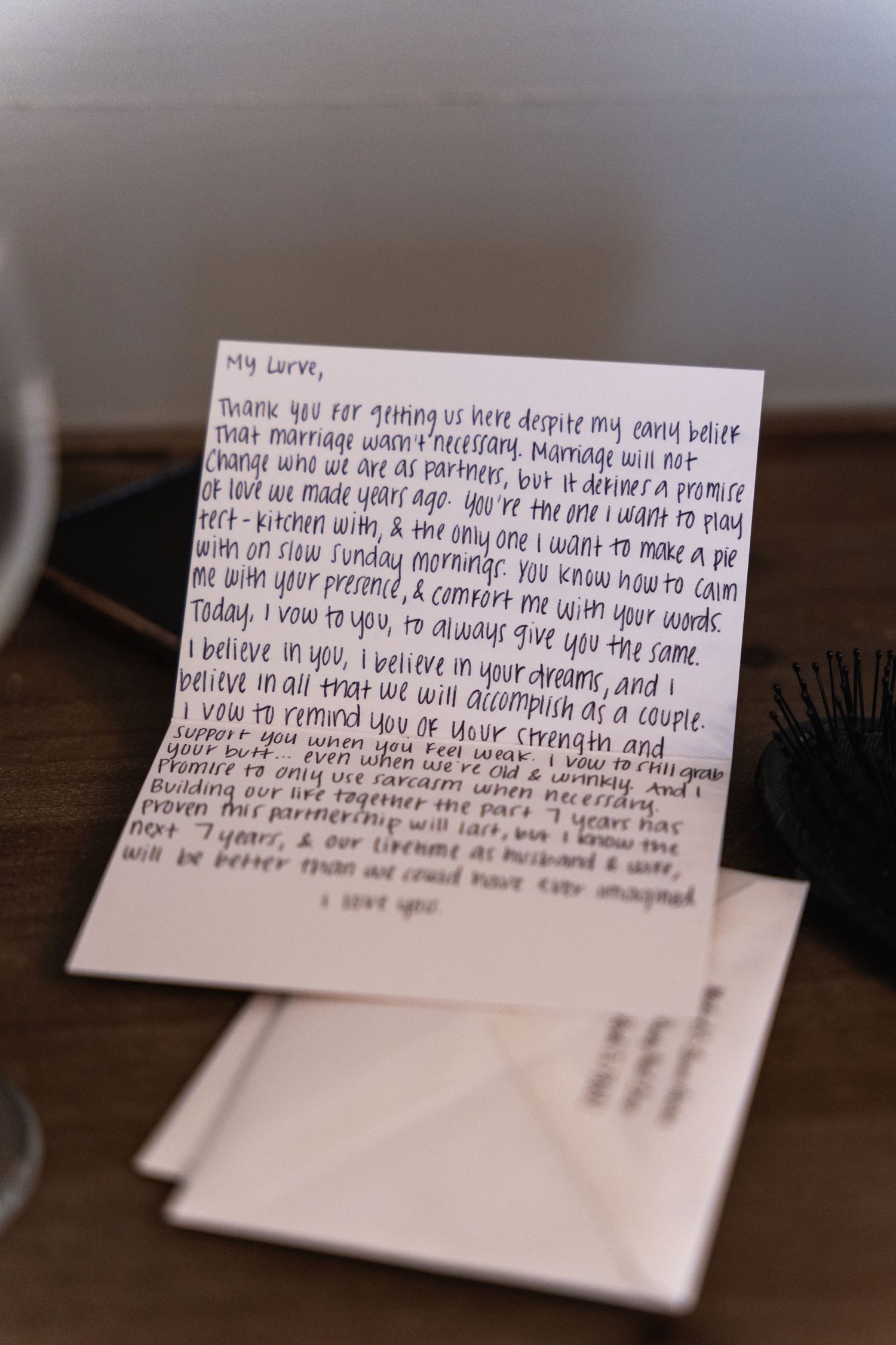 Handwritten letter on white paper sitting on wooden surface in soft focus.