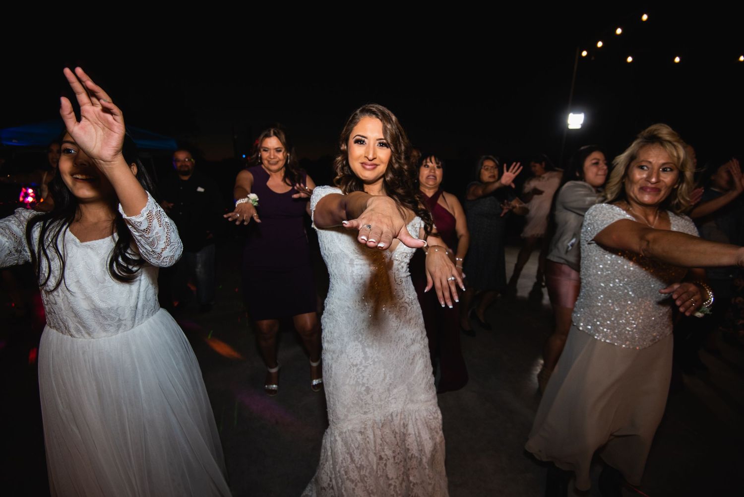 Wedding guests performing choreographed dance moves at outdoor nighttime reception.