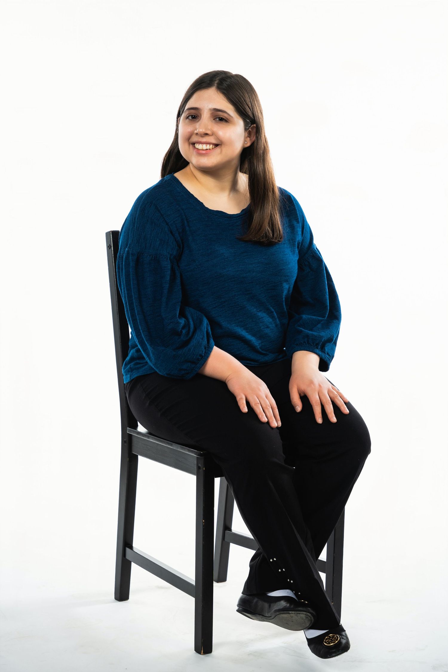 Woman in navy blue top sitting on black chair against white background.
