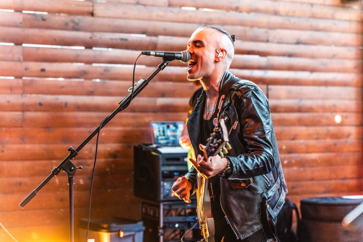 Performer singing passionately into microphone while playing guitar on wooden stage.