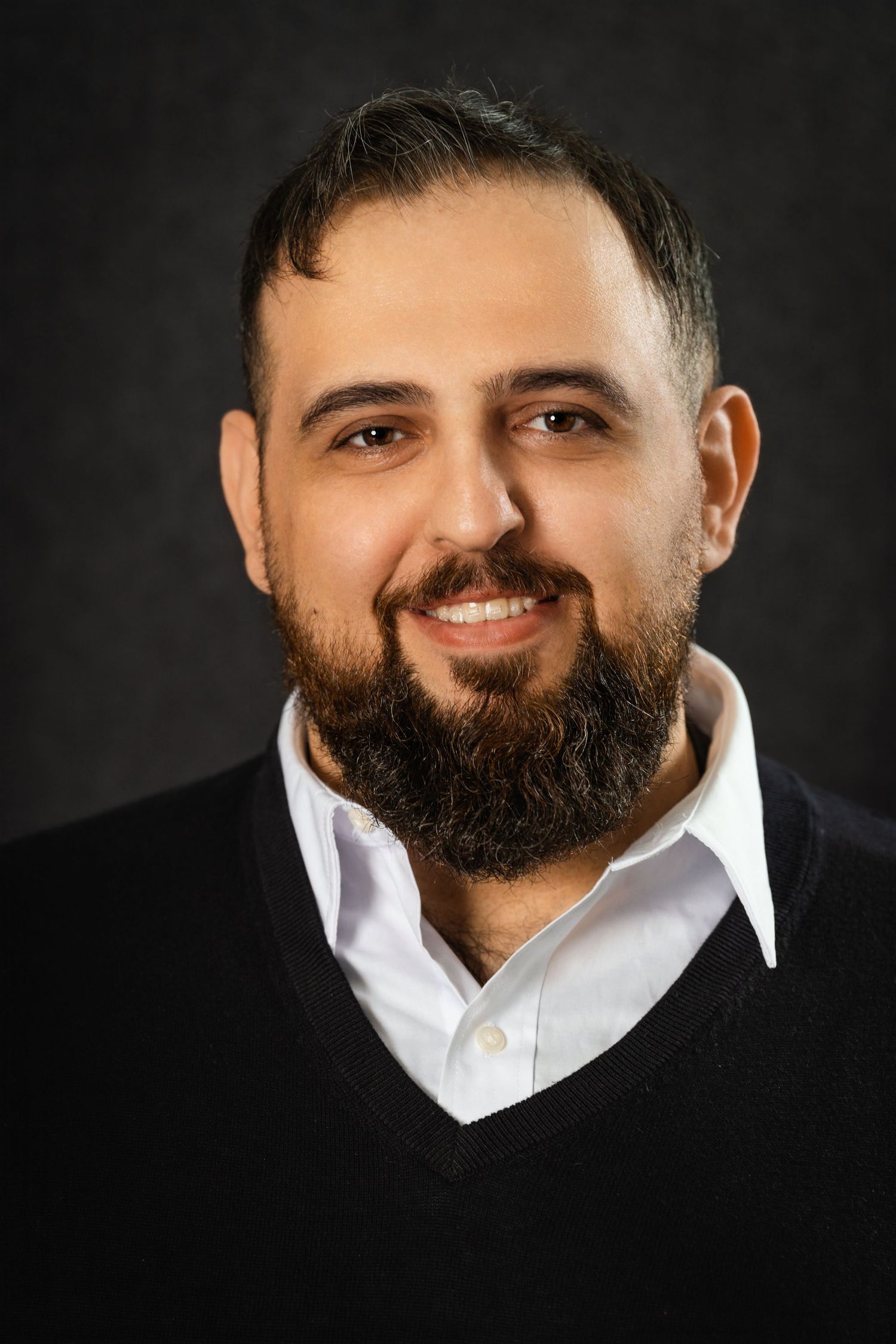 Professional studio portrait of man in black sweater and white shirt.