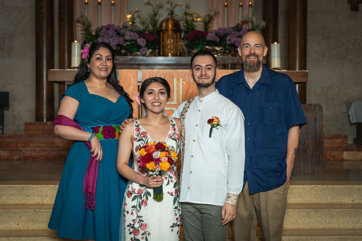 Small group poses on church steps during wedding ceremony wearing colorful attire.