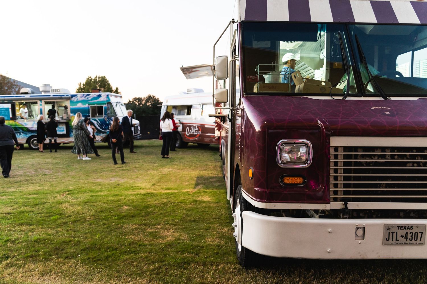 Food trucks and vendors line up on grass at an outdoor event venue.