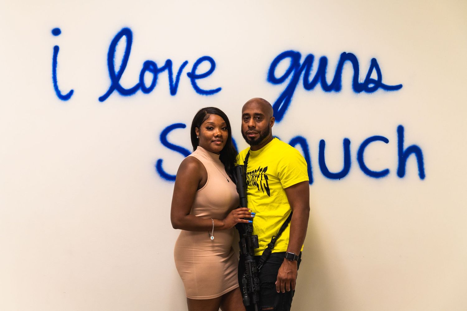 Couple posing together in front of blue text wall at shooting range.