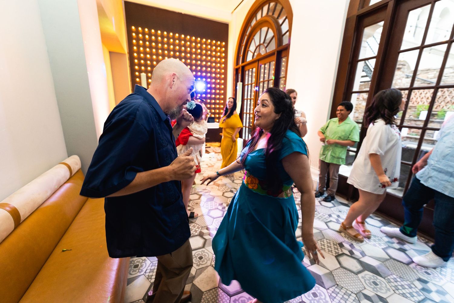 People dancing and celebrating in a venue with yellow walls and decorative windows.