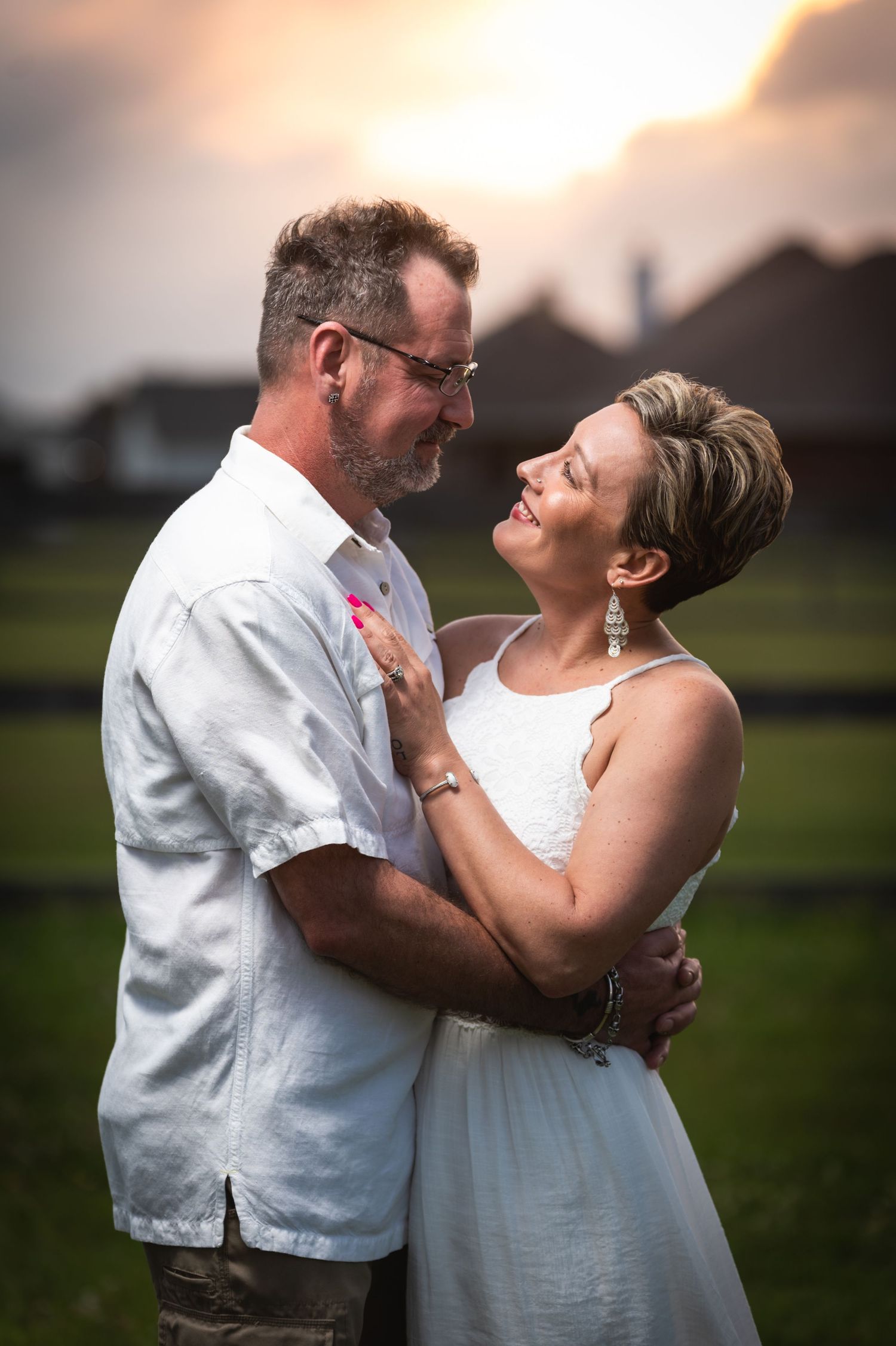 Intimate portrait of couple embracing in white outfits during sunset.
